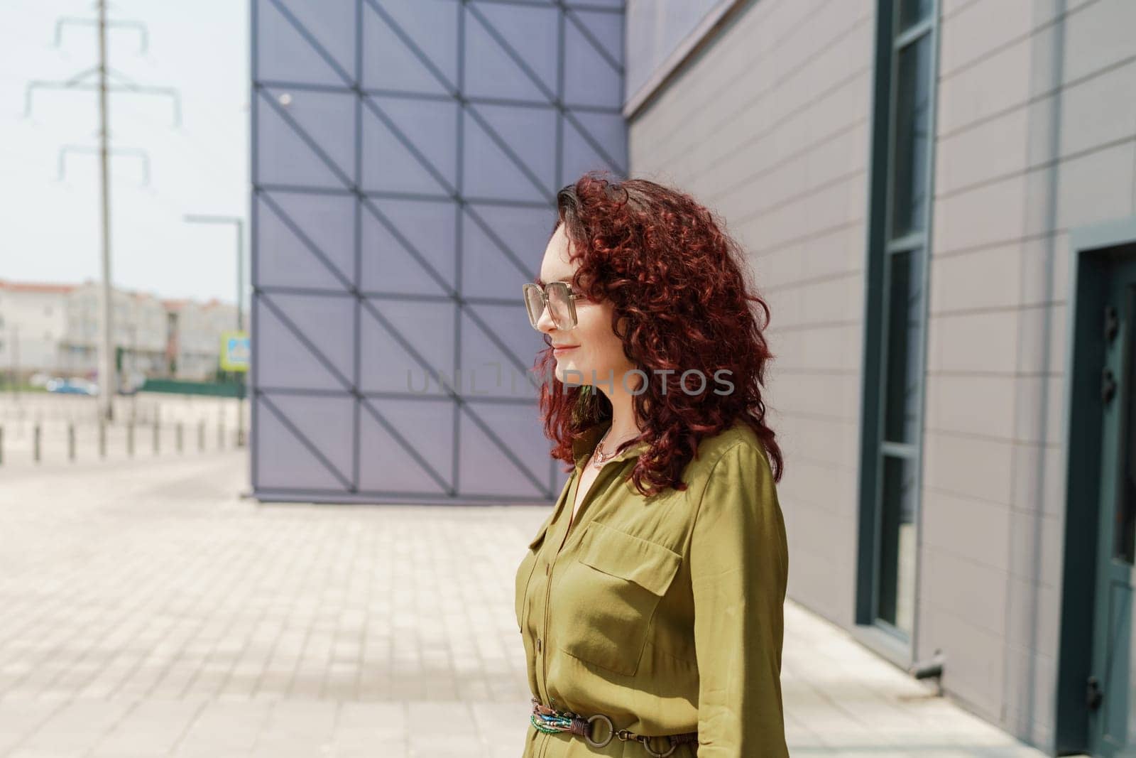 Portrait of a woman standing near a supermarket building. Caucasian model with long brunette hair, wears sunglasses and a khaki dress