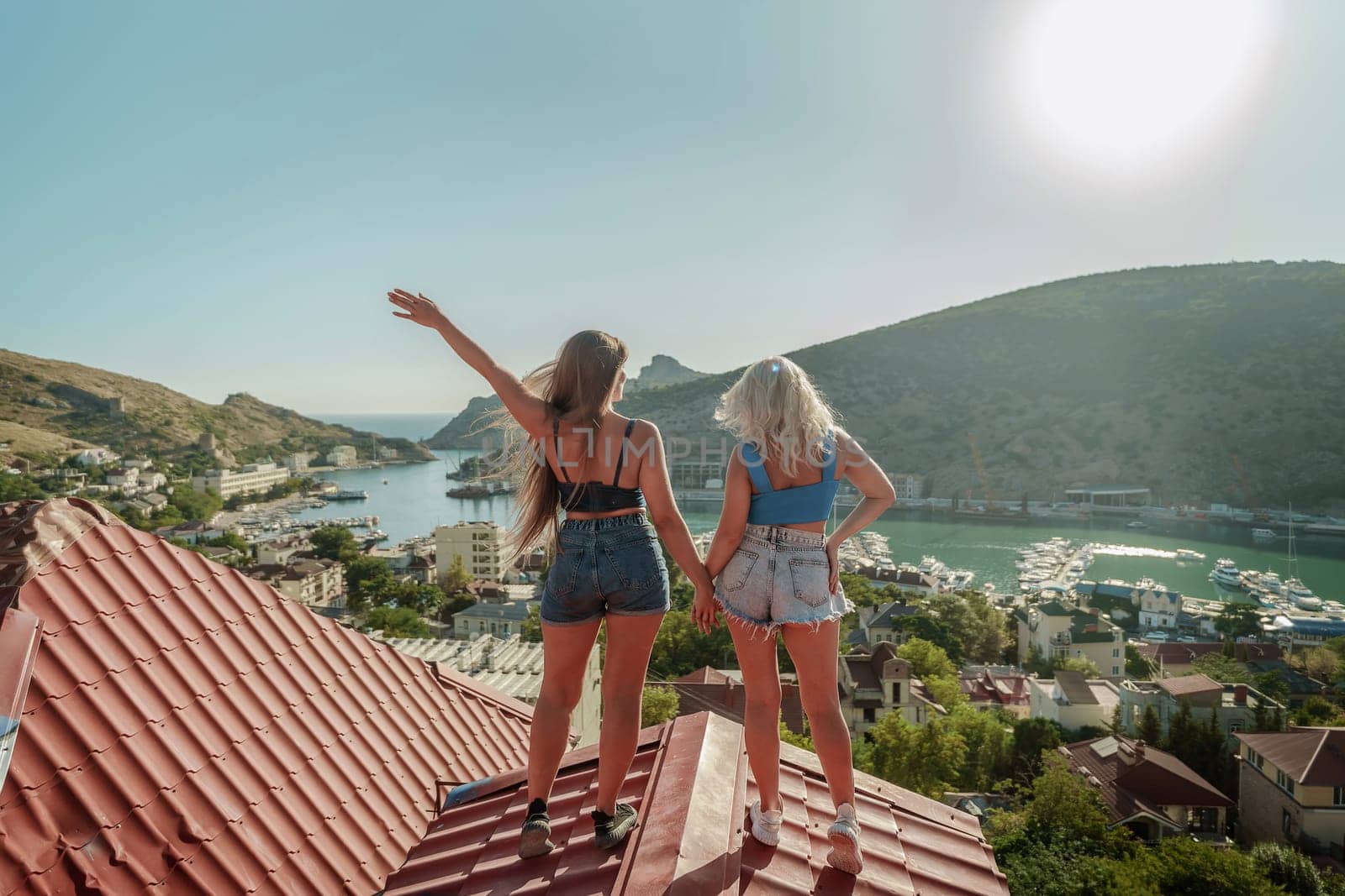 women standing on rooftop, enjoys town view and sea mountains. Peaceful rooftop relaxation. Below her, there is a town with several boats visible in the water. Rooftop vantage point. by Matiunina