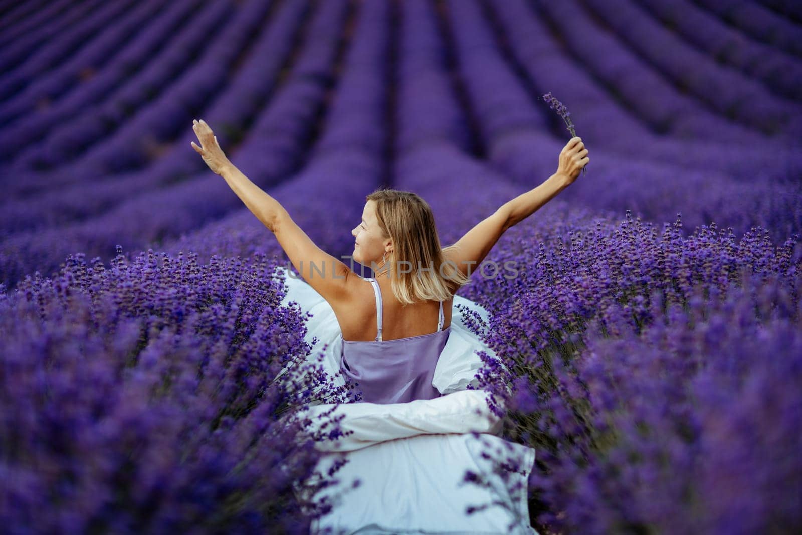 A middle-aged woman sits in a lavender field and enjoys aromatherapy. Aromatherapy concept, lavender oil, photo session in lavender.