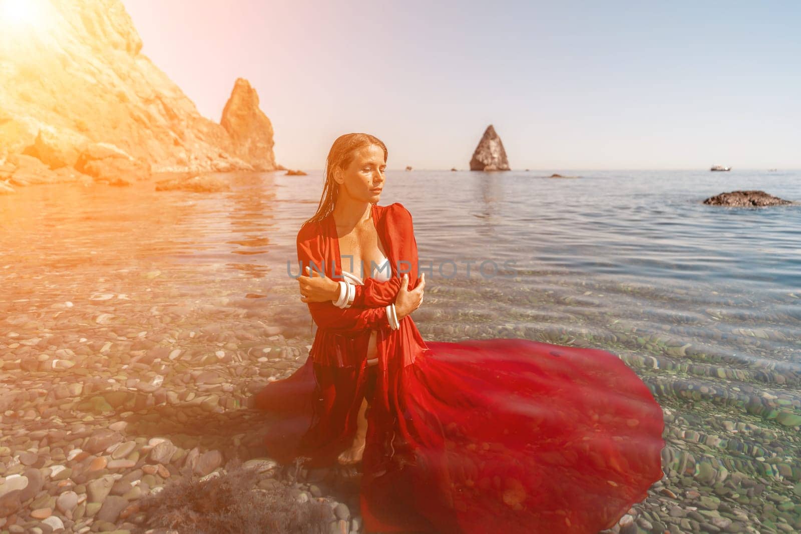 woman sea red dress. Beautiful sensual woman in a flying red dress and long hair, standing in sea in a large bay