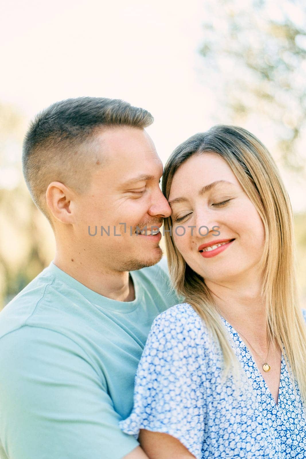 Guy hugs girl from behind, touching her forehead with his nose in the garden by Nadtochiy