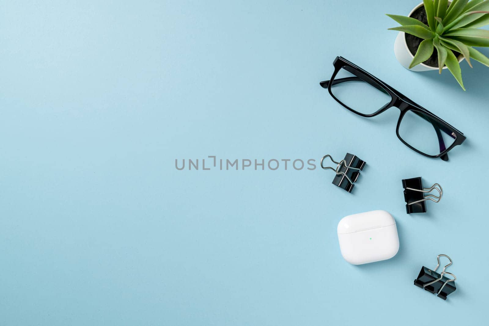 Top view of Glasses, black binder paper clip and headphones on blue table by Sonat