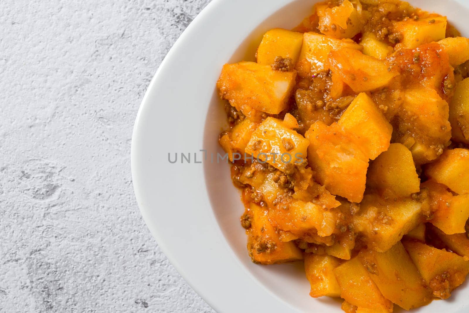 Minced meat and potato dish on white porcelain plate on stone table by Sonat