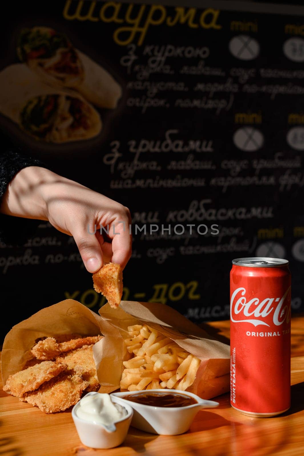 Ivano-Frankivsk, Ukraine March 26, 2023: Female hand dips chicken nuggets in sauce by Niko_Cingaryuk