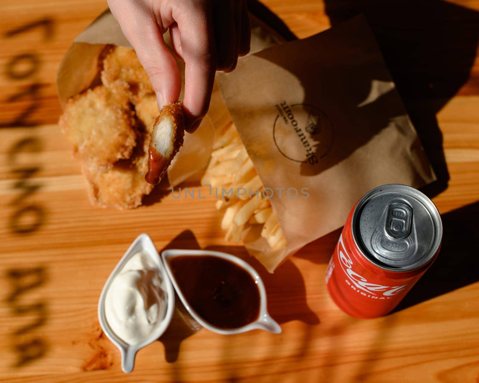 Ivano-Frankivsk, Ukraine March 26, 2023: Female hand dips chicken nuggets in sauce by Niko_Cingaryuk