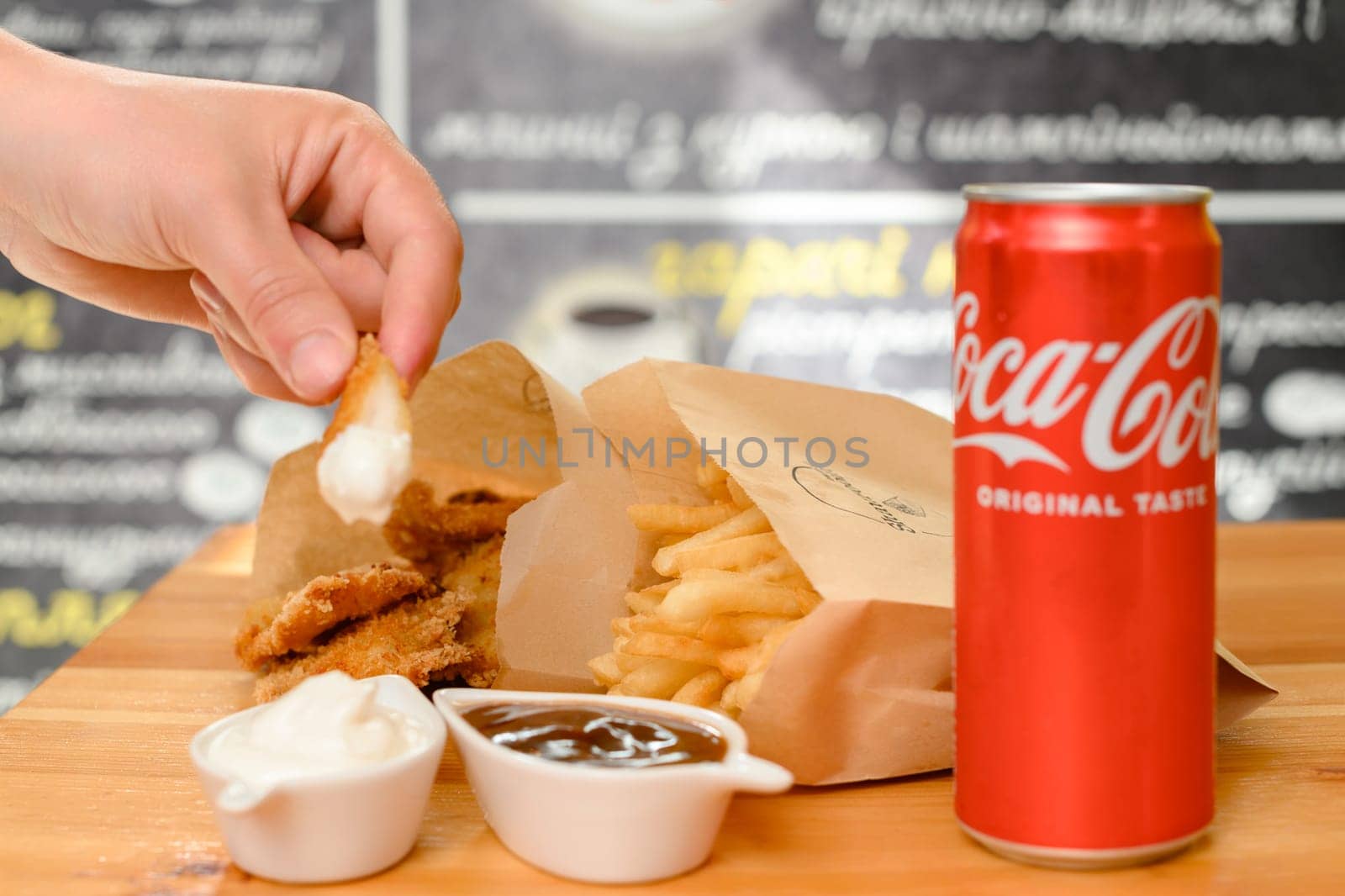 Ivano-Frankivsk, Ukraine March 26, 2023: Female hand dips chicken nuggets in sauce, chicken nuggets, french fries and coca cola on the table.