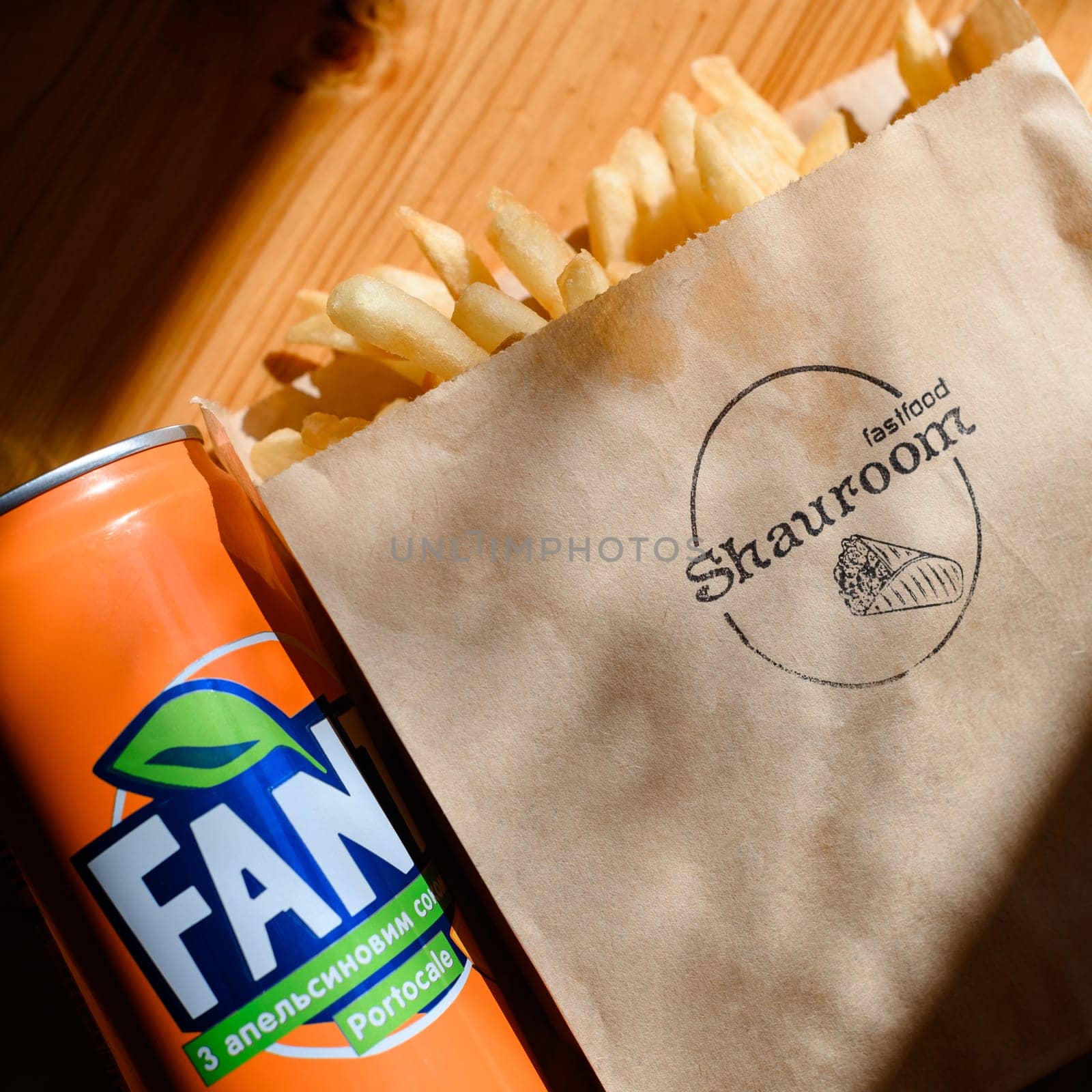 Ivano-Frankivsk, Ukraine March 26, 2023: Fanta and french fries in a branded paper bag on a table illuminated by the window.