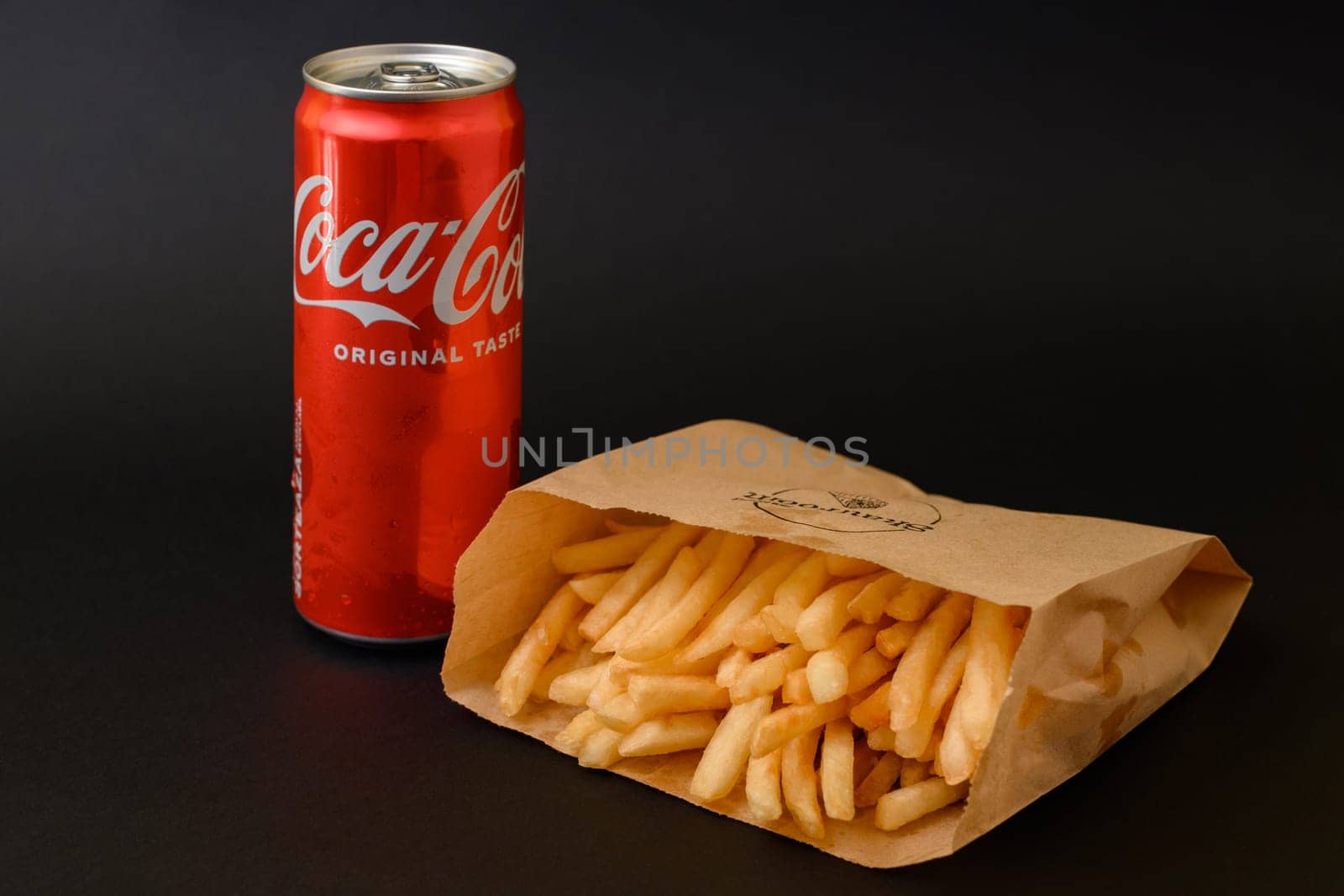 Ivano-Frankivsk, Ukraine March 26, 2023: Coca Cola and french fries in a paper bag on a black background.