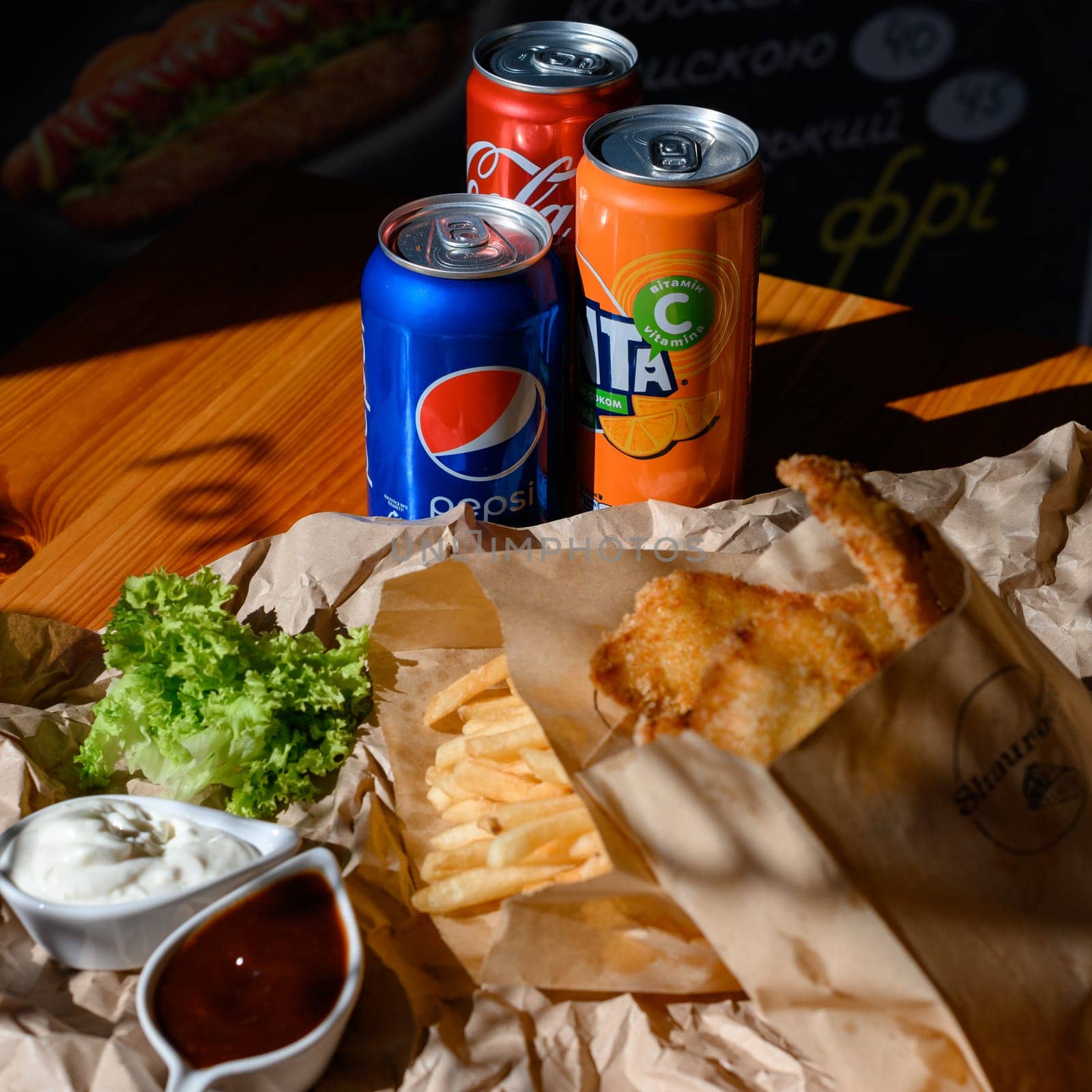 Ivano-Frankivsk, Ukraine March 26, 2023: three bottles of coke, fanta and pepsi with chicken nuggets and french fries on the table, fatty and unhealthy food.