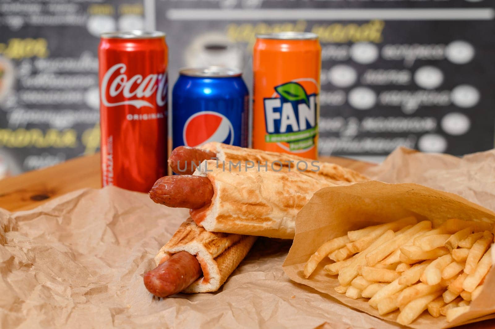 Ivano-Frankivsk, Ukraine March 26, 2023: three bottles of coke, fanta and pepsi with hotdogs and french fries on the table, fatty and unhealthy food.
