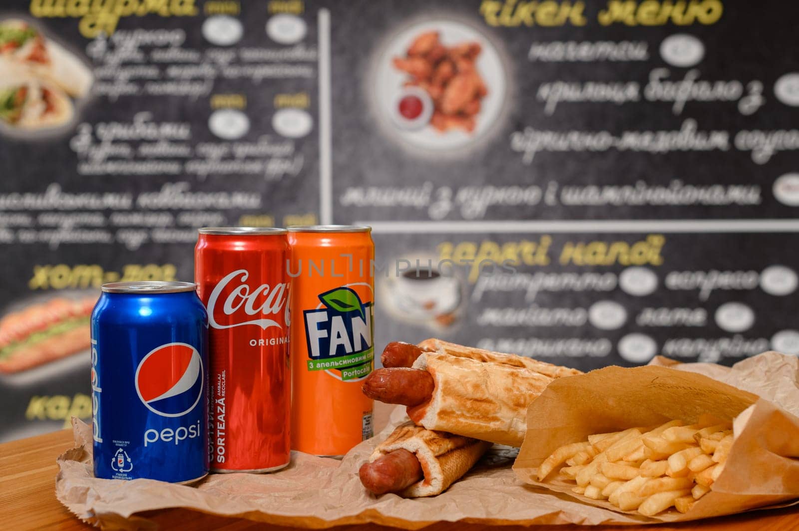 Ivano-Frankivsk, Ukraine March 26, 2023: three bottles of coke, fanta and pepsi with hotdogs and french fries on the table. by Niko_Cingaryuk