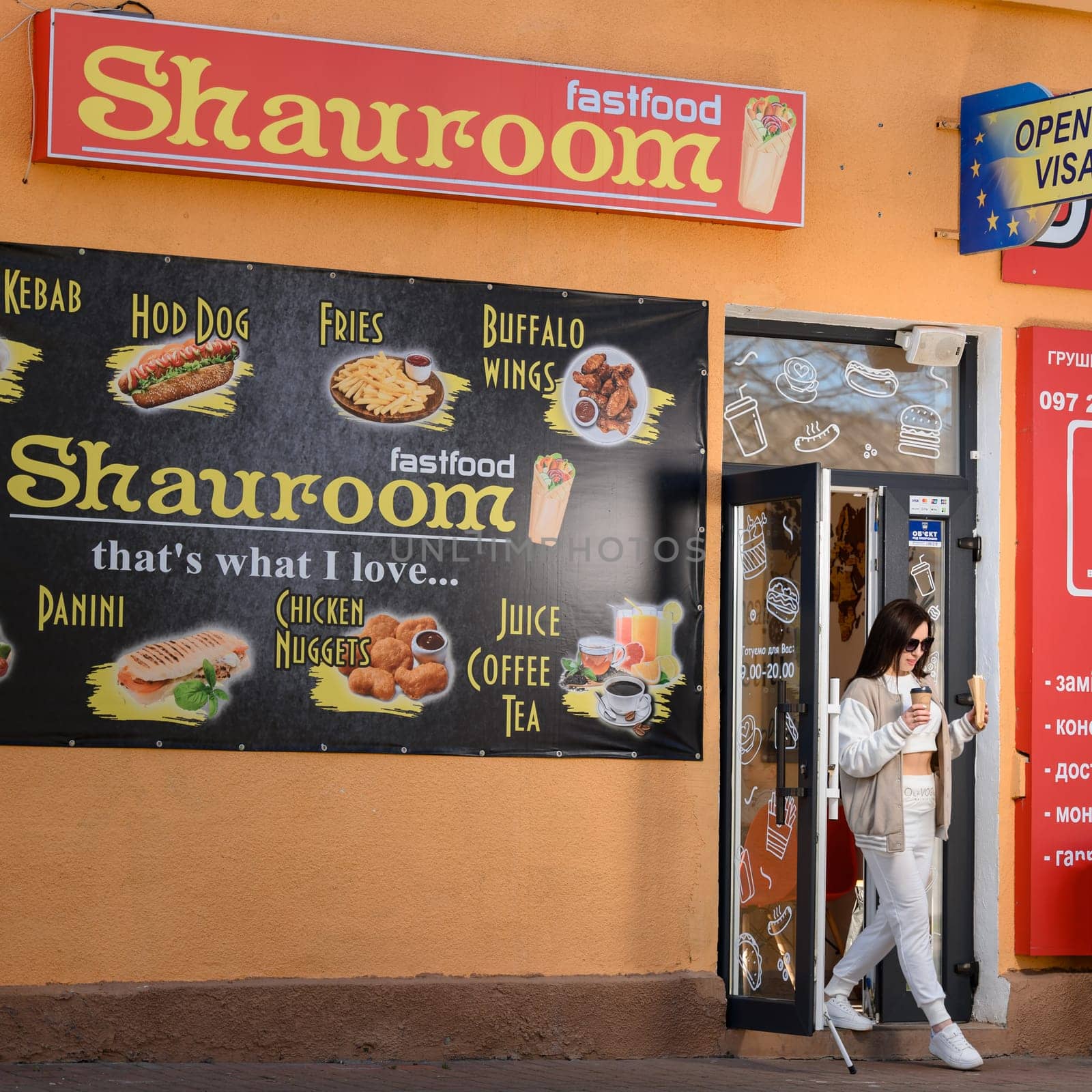 Ivano-Frankivsk, Ukraine March 26, 2023: a girl comes out of a cafe and holds coffee and shawarma in her hands, walking with food.