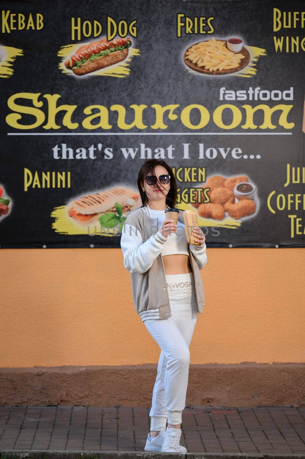 Ivano-Frankivsk, Ukraine March 26, 2023: a girl comes out of a cafe and holds coffee and shawarma in her hands, walking with food.