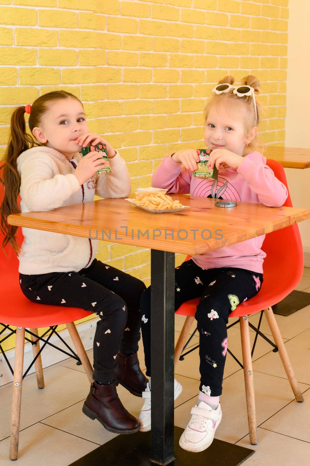 Ivano-Frankivsk, Ukraine March 26, 2023: two little girls in a cafe drinking juice and eating fries, children in a cafe.