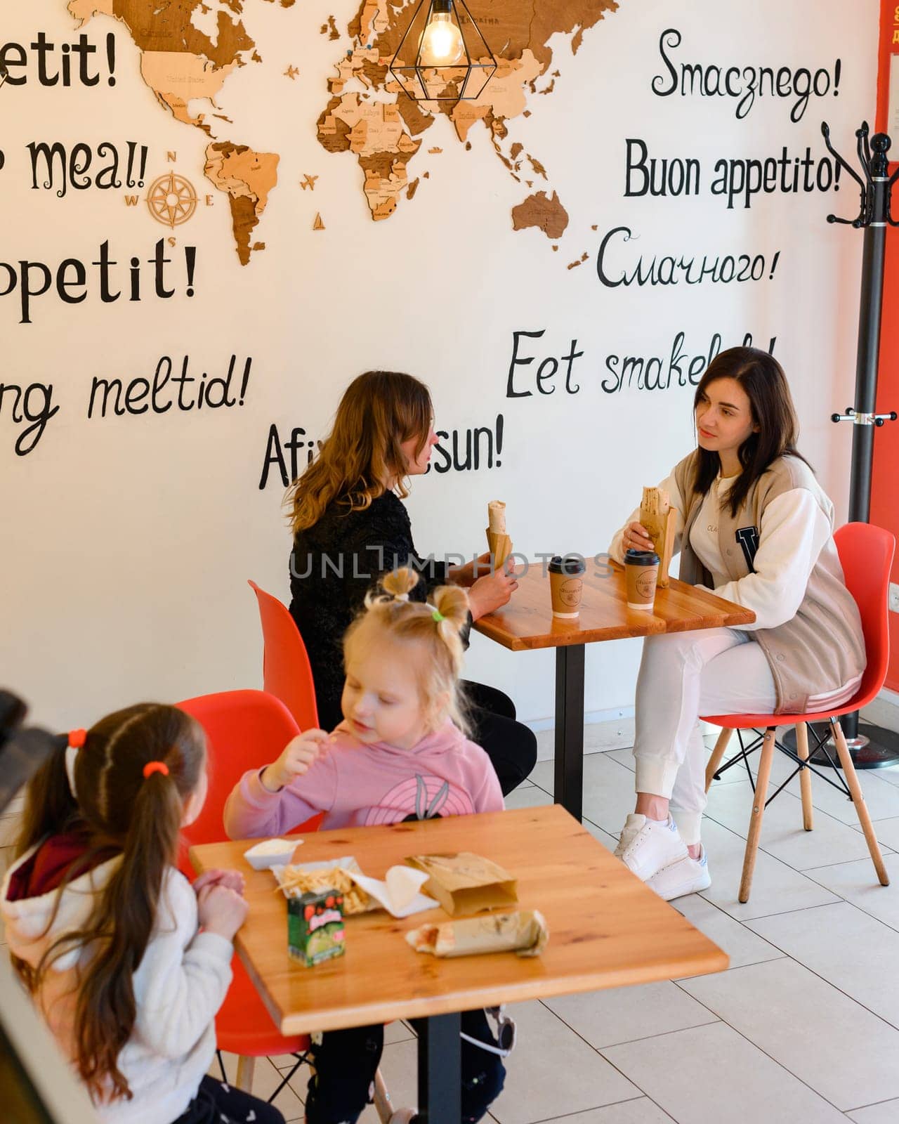 Ivano-Frankivsk, Ukraine March 26, 2023: two mothers and their daughters sit in a cafe and hold shawarma and coffee in their hands, a meeting of friends in a cafe.