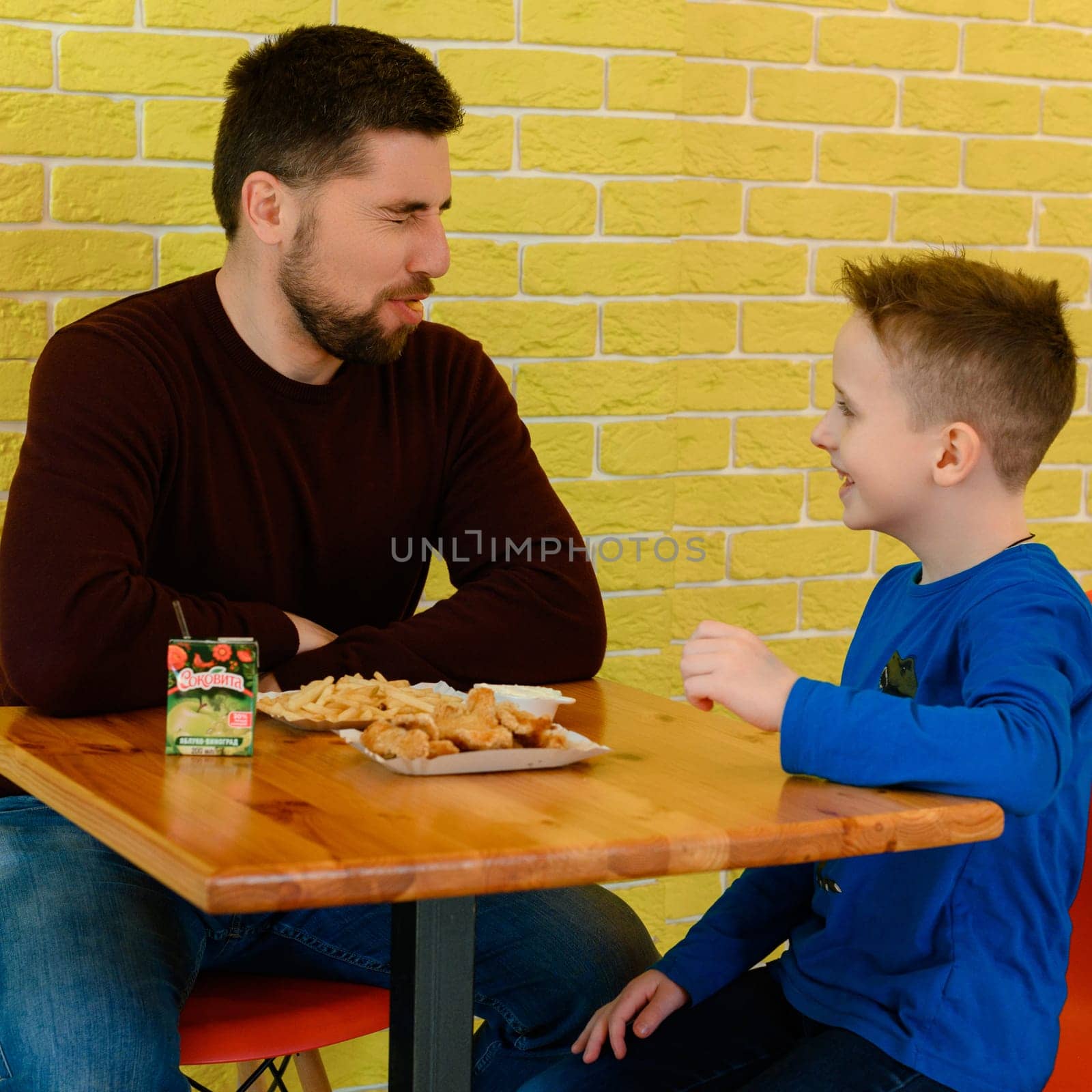 Ivano-Frankivsk, Ukraine March 26, 2023: A father and son eat chicken nuggets and French fries in a cafe. by Niko_Cingaryuk