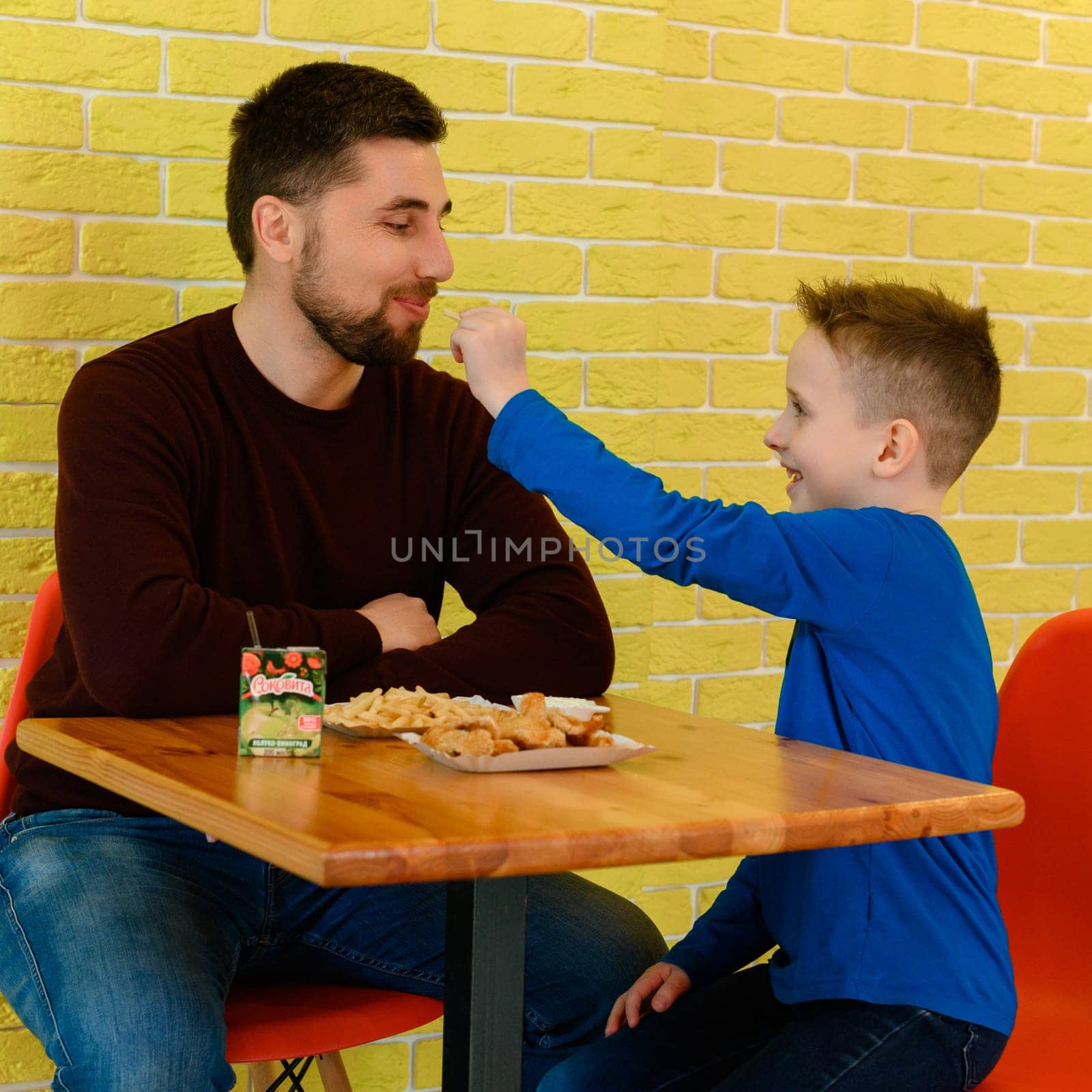 Ivano-Frankivsk, Ukraine March 26, 2023: A father and son eat chicken nuggets and French fries in a cafe. by Niko_Cingaryuk