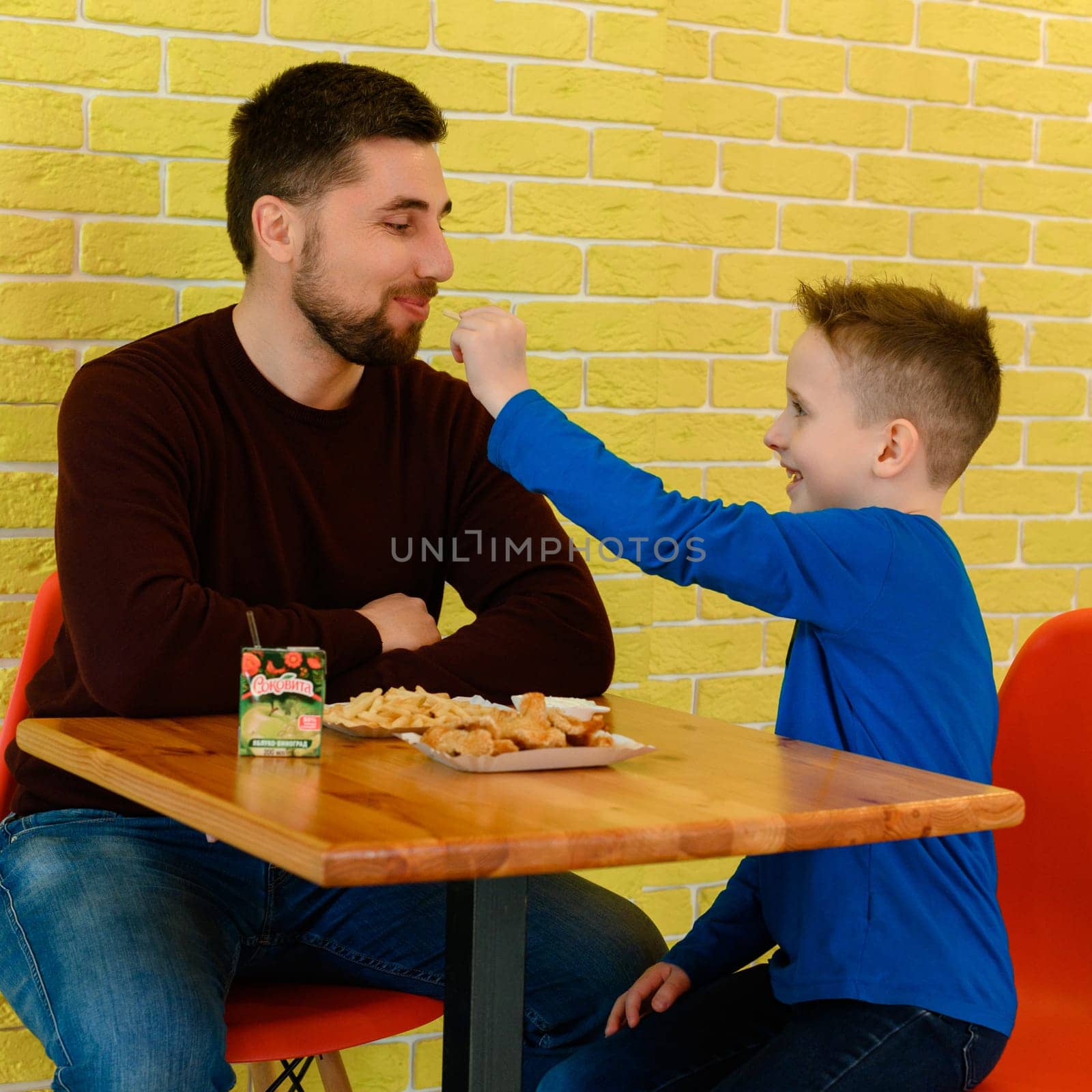 Ivano-Frankivsk, Ukraine March 26, 2023: A father and son eat chicken nuggets and French fries in a cafe.