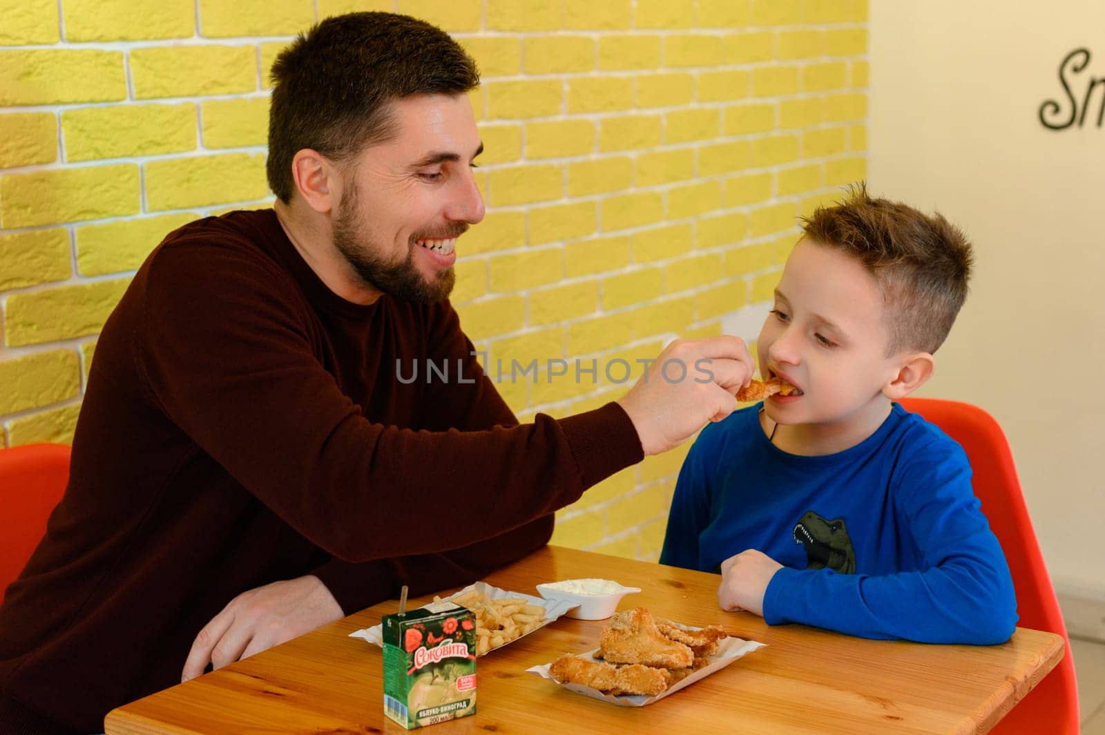 Ivano-Frankivsk, Ukraine March 26, 2023: A father and son eat chicken nuggets and French fries in a cafe. by Niko_Cingaryuk