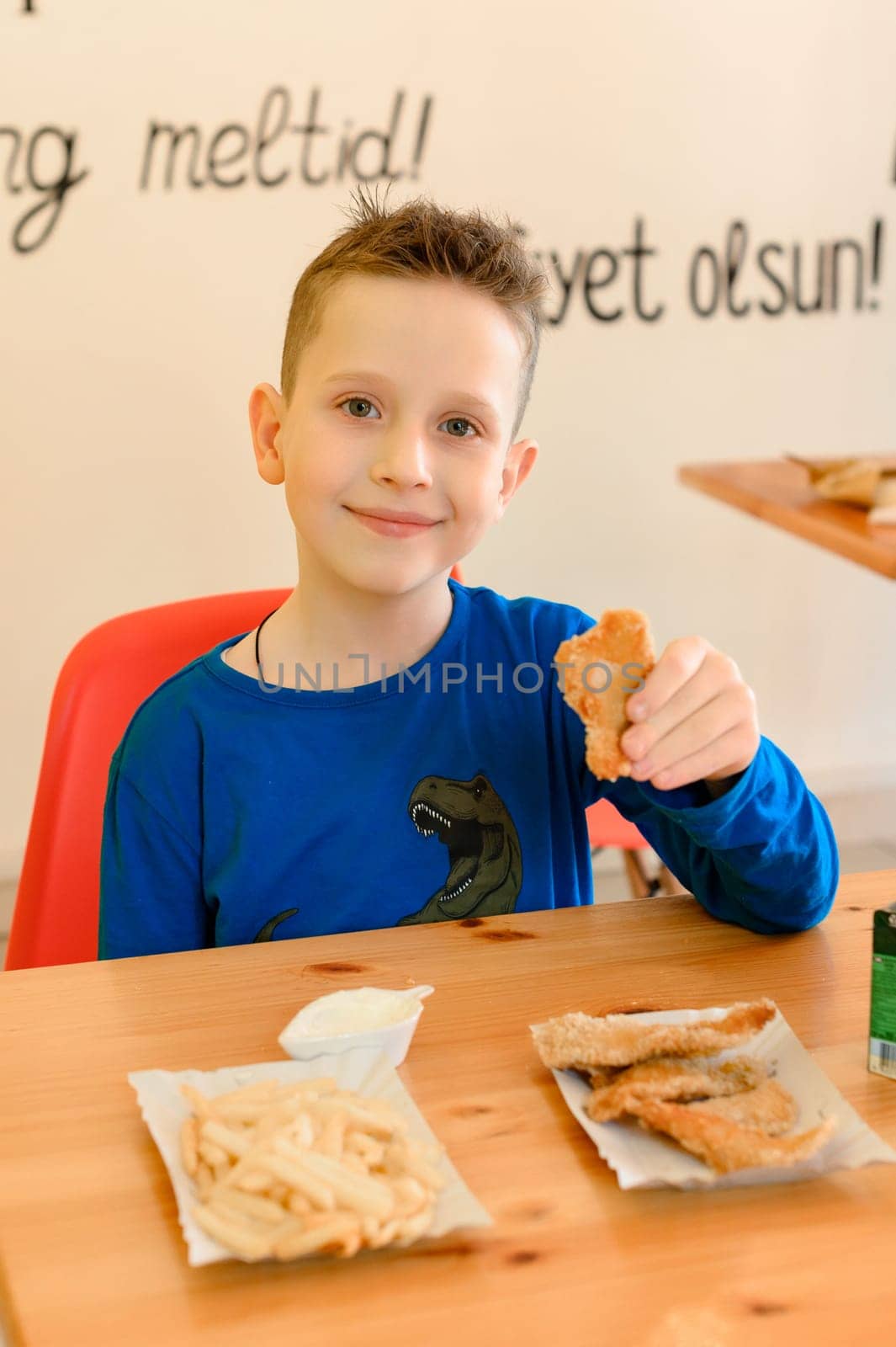 Ivano-Frankivsk, Ukraine March 26, 2023: little smiling boy eating chicken nuggets in a cafe by Niko_Cingaryuk