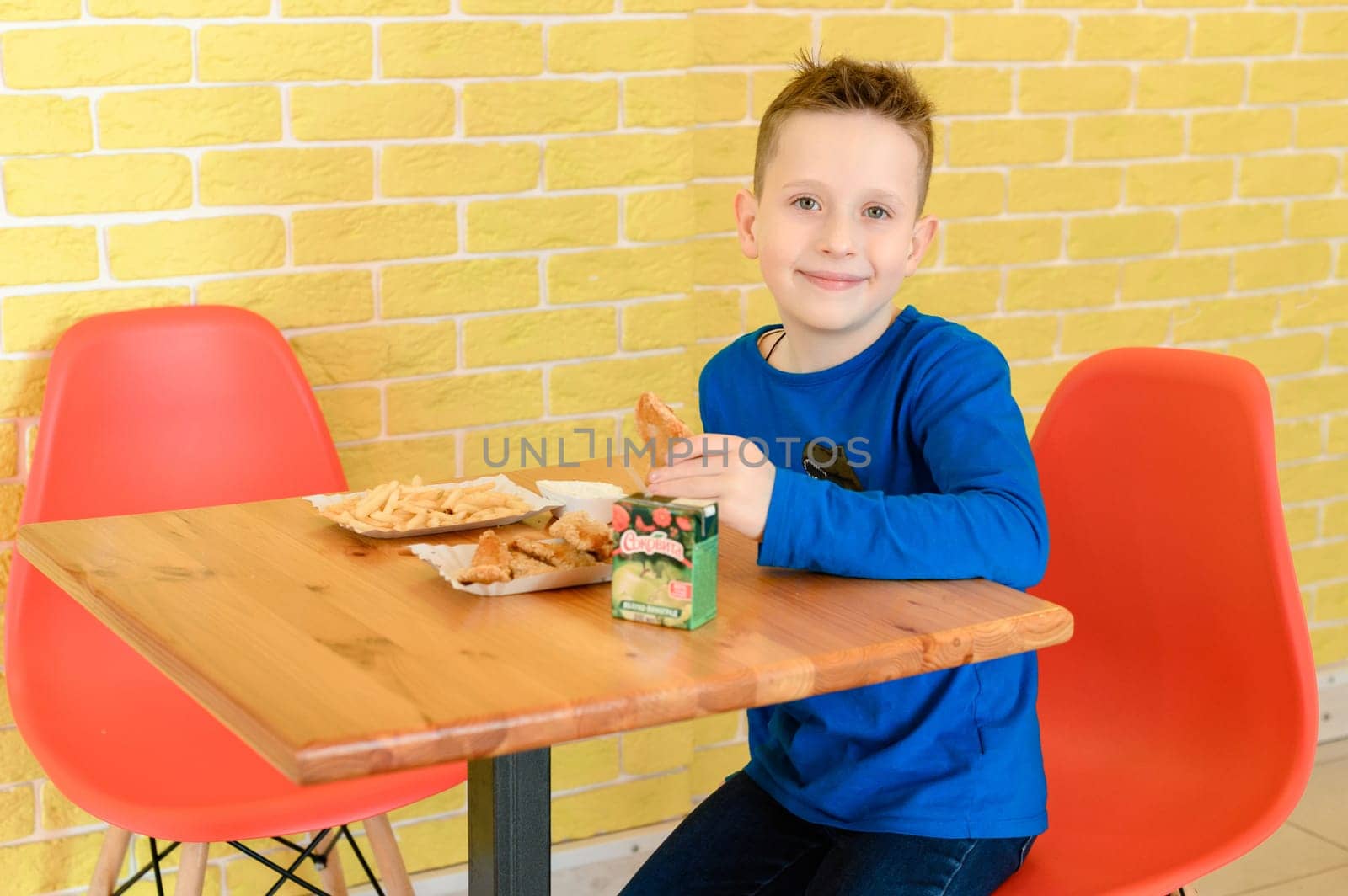 Ivano-Frankivsk, Ukraine March 26, 2023: little smiling boy eating chicken nuggets in a cafe by Niko_Cingaryuk