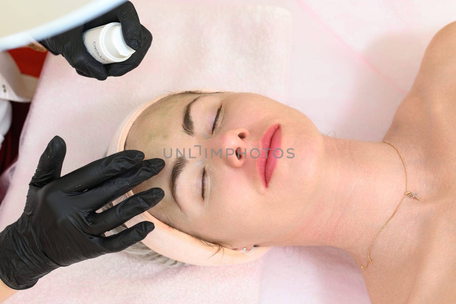 Ivano-Frankivsk, Ukraine May 17, 2023: A beautician applies a green mask to a girl's face, carboxytherapy cosmetology procedure, a beautician in black gloves.