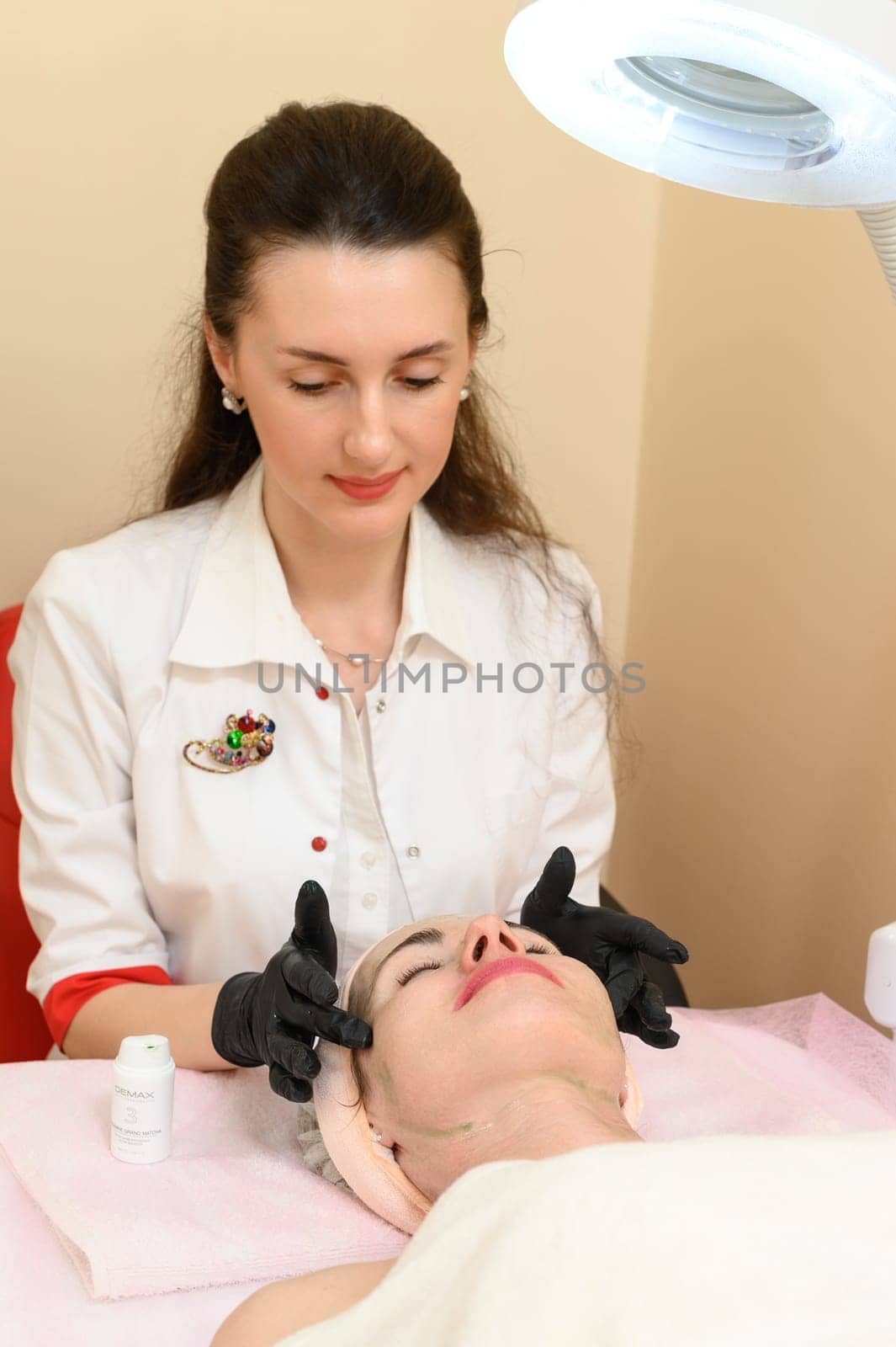 Ivano-Frankivsk, Ukraine May 17, 2023: Rubbing the cream with massage movements on the face, therapy at a beautician by Niko_Cingaryuk