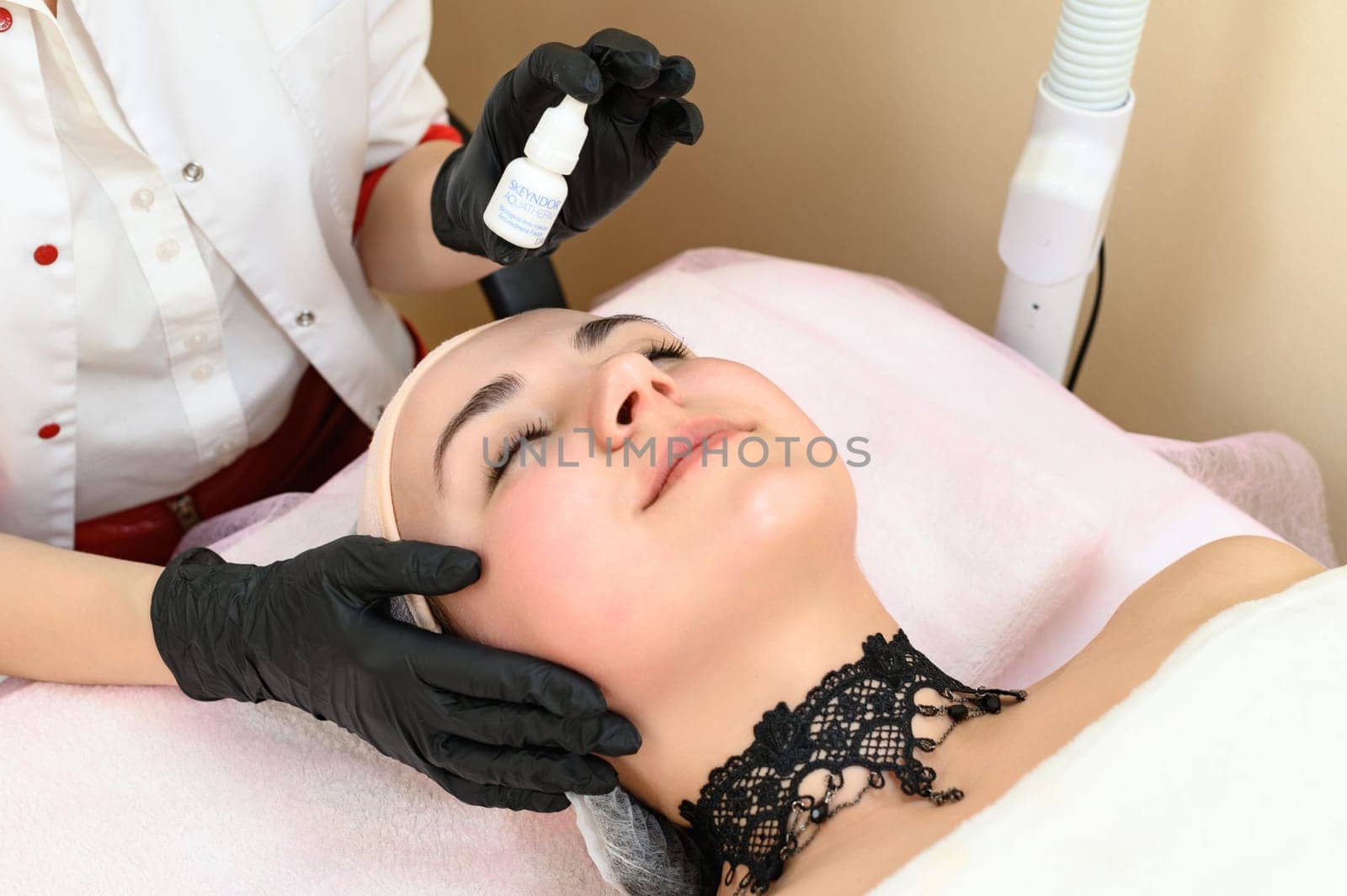 A beautician applies cream against couperosis to a girl's face. Ivano-Frankivsk, Ukraine May 17, 2023 by Niko_Cingaryuk