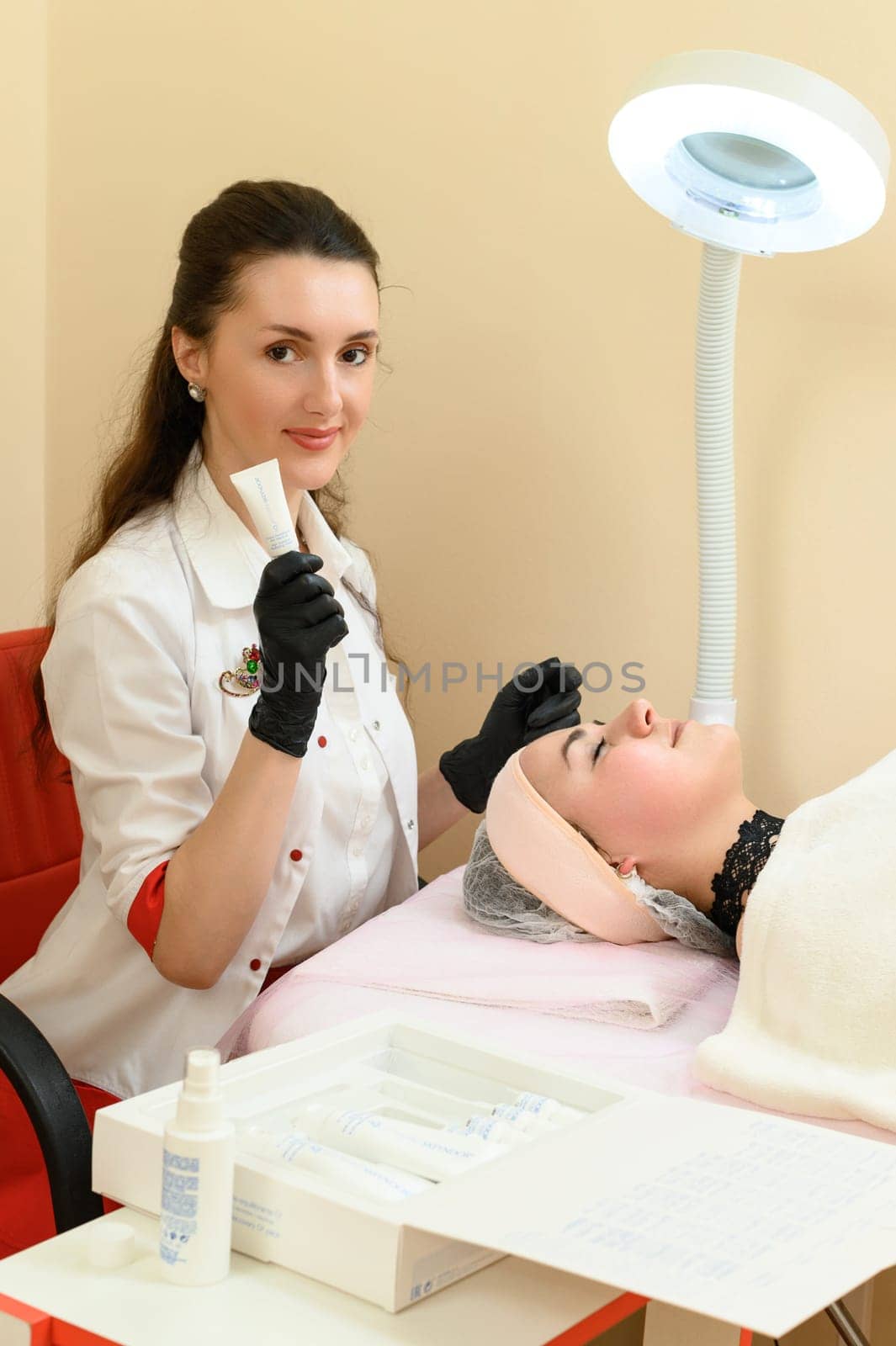 The cosmetologist demonstrates the cream that will be used for the procedure, the cosmetologist and the patient girl. Ivano-Frankivsk, Ukraine May 17, 2023