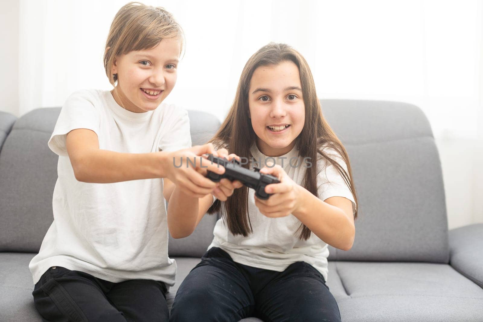 Two little girlfriends playing video game with joysticks. Excited and focused european children. Childhood concept. Entertainment and leisure. Idea of friendship. Grey background in studio. Copy space by Andelov13