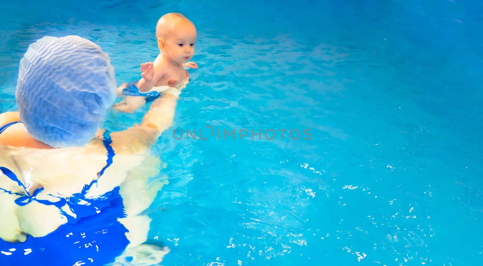 Adorable baby girl enjoying swimming in a pool with her mother early development class for infants teaching children to swim and dive. Swimming instructor doing exercises with a small child in the pool . High quality photo