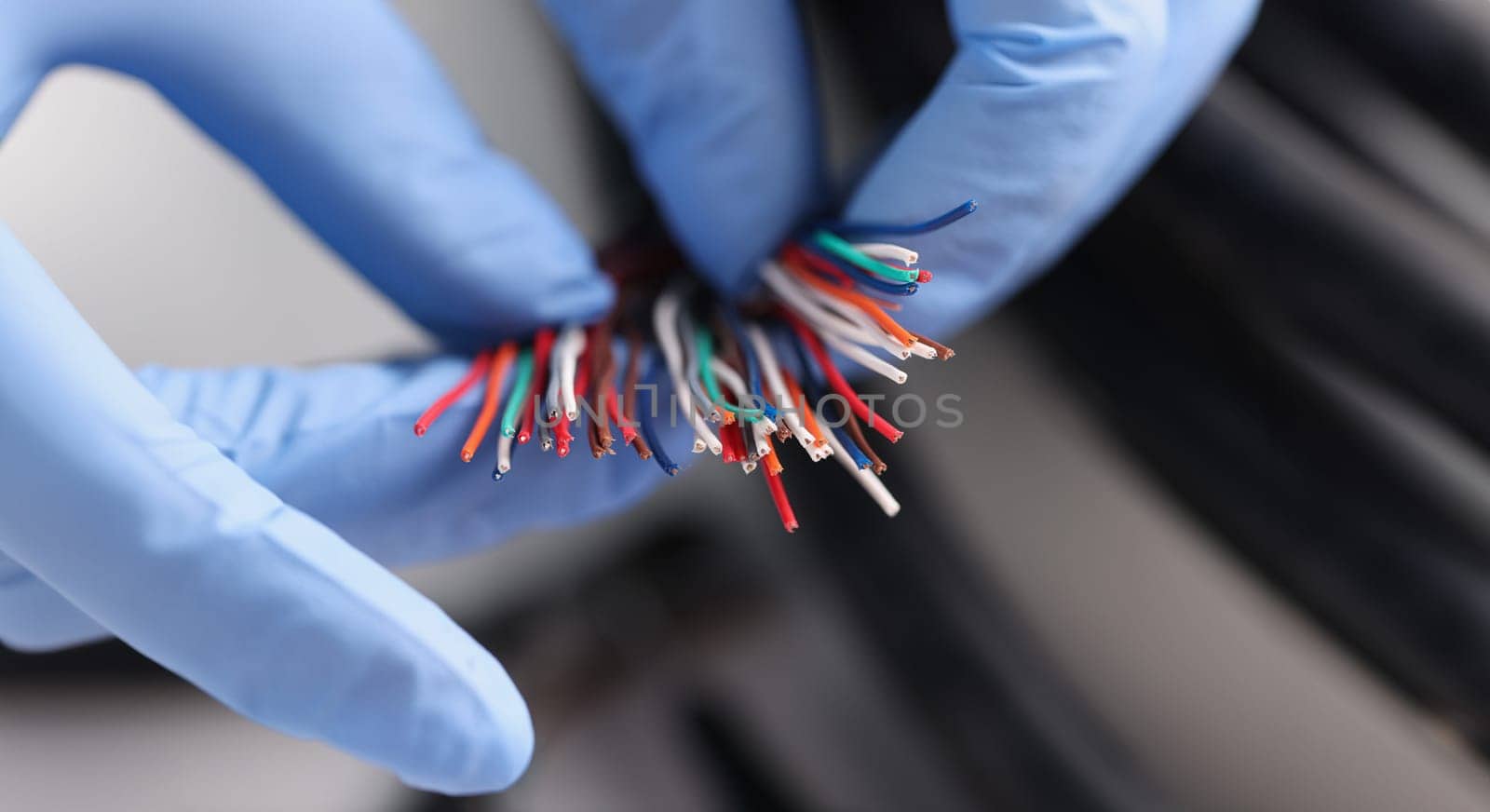 Gloved master holds colored electronic wires. Electrician services concept