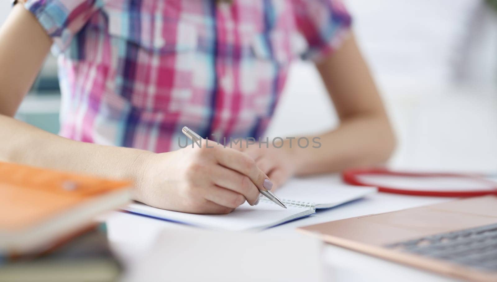 Woman's hand makes notes with pen in notebook. Remote education concept