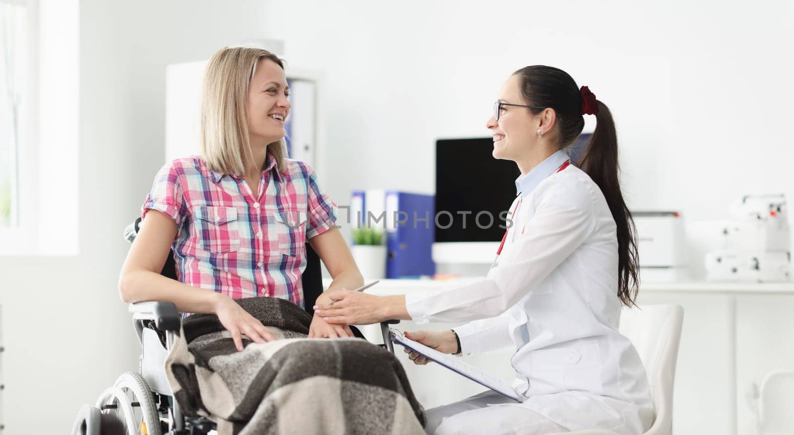 Smiling doctor communicates with patient in wheelchair. Medical rehabilitation of disabled people concept