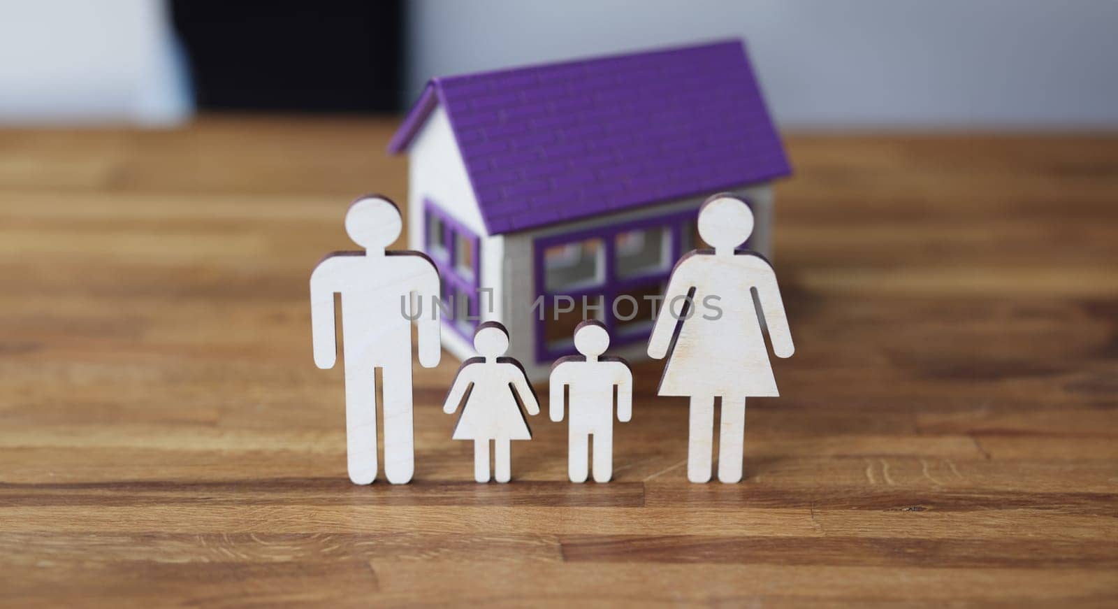 Wooden figurines of parents and children on background of house. Receiving social housing concept