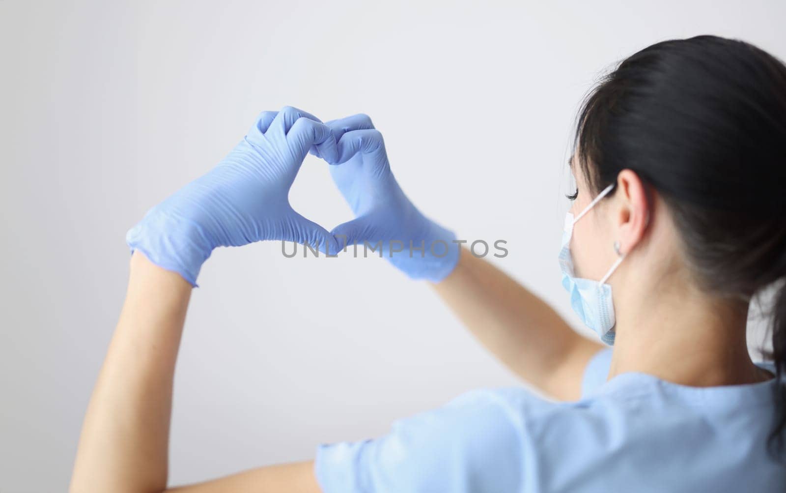 Doctor in medical protective mask and gloves holds his hands in shape of heart. Healthcare and fight against coronavirus pandemic concept