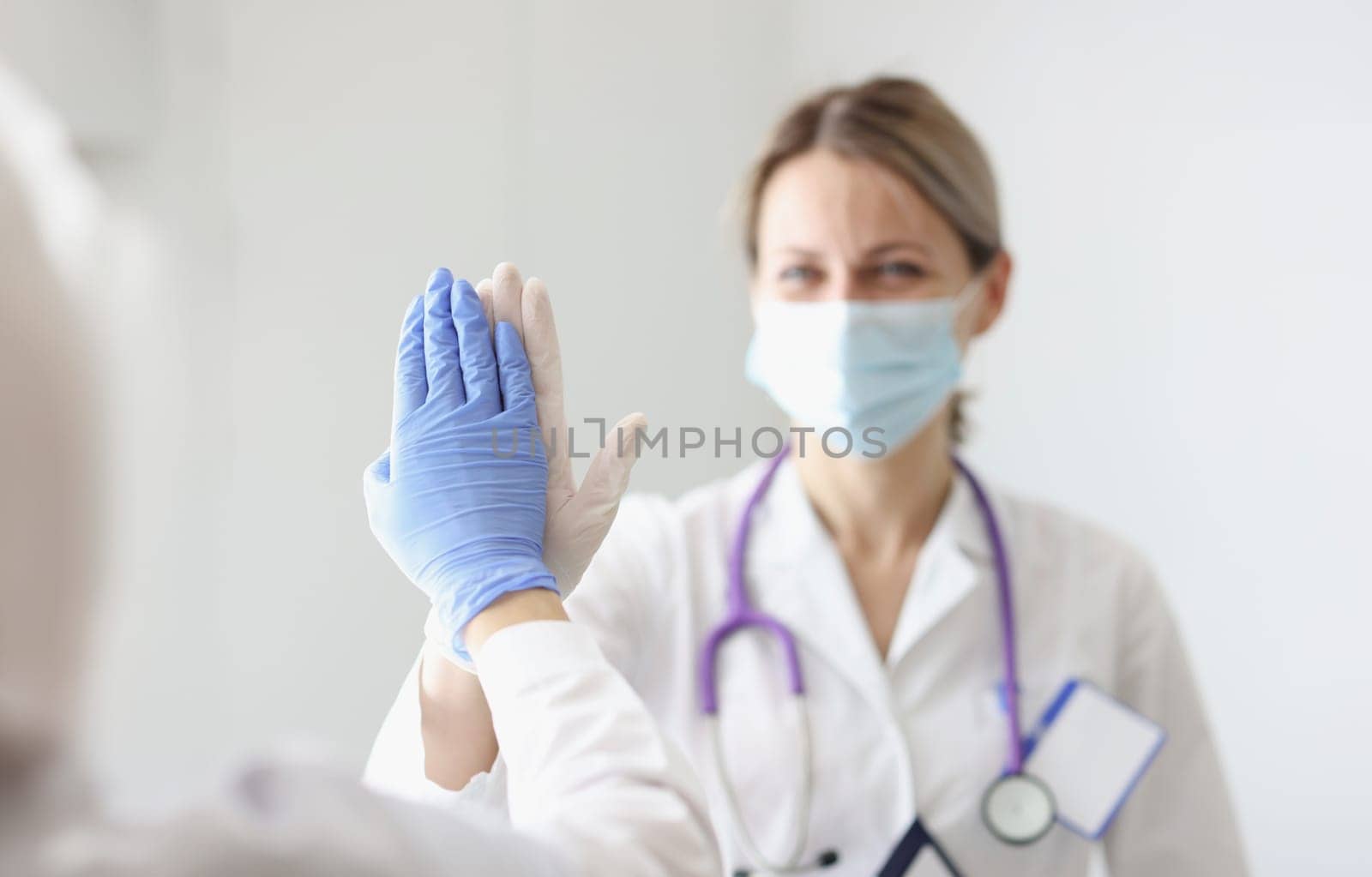 Two doctors in protective masks and gloves give each other five. Successful method of treating patients concept