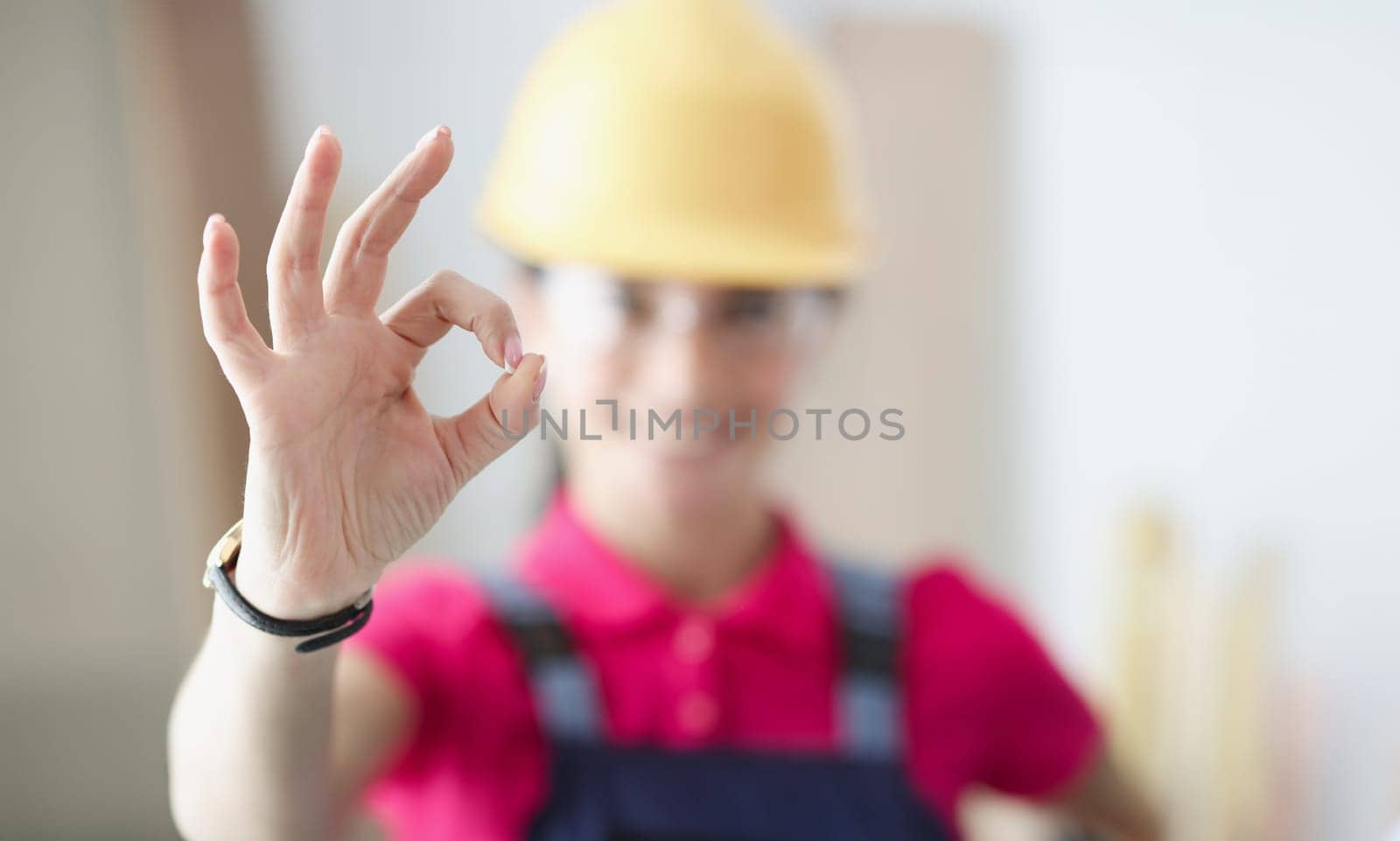 Smiling woman builder holds thumbs up in gesture ok. Housing construction concept