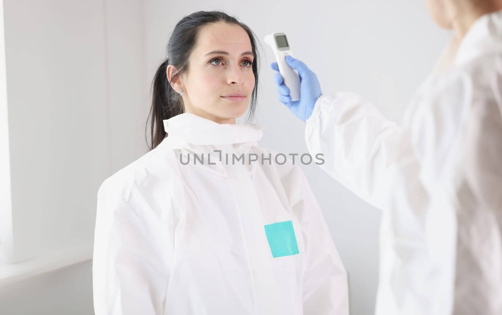 For doctor in protective suit, body temperature is measured with thermometer after work shift by kuprevich