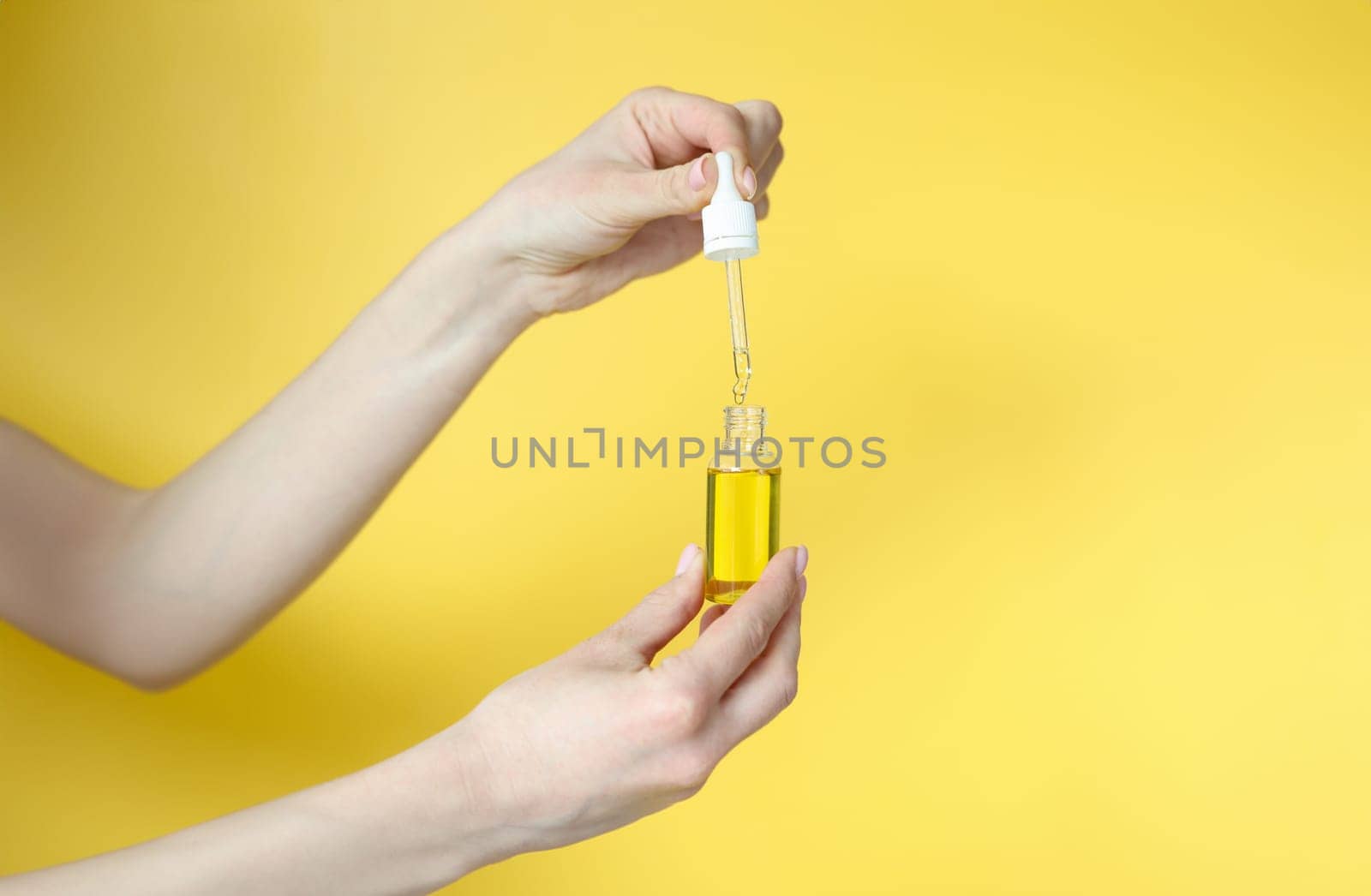 Woman holding cosmetic oil in her hands on yellow background closeup. Aromatherapy concept