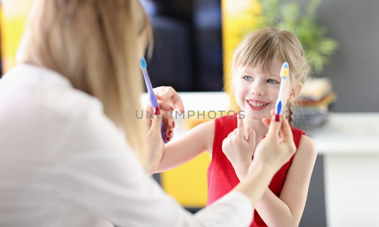 Little girl choosing toothbrush from doctors hands in clinic by kuprevich