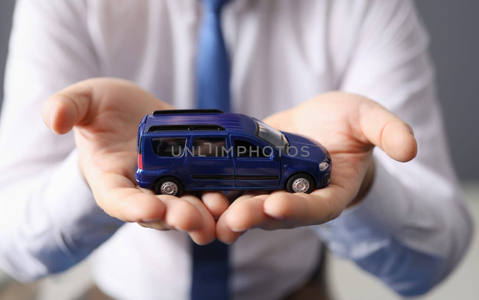Man holding blue toy car in his hands closeup. Car insurance concept