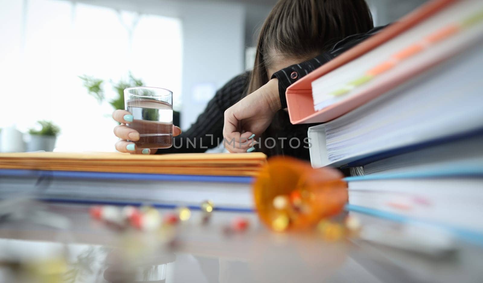 Tired woman lying on folders with glass of water in her hand. Paperwork concept