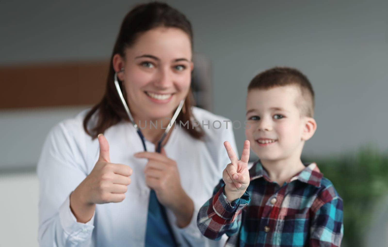 Young smiling doctor and child showing thumbs up closeup. Pediatrics examination and treatment of children concept