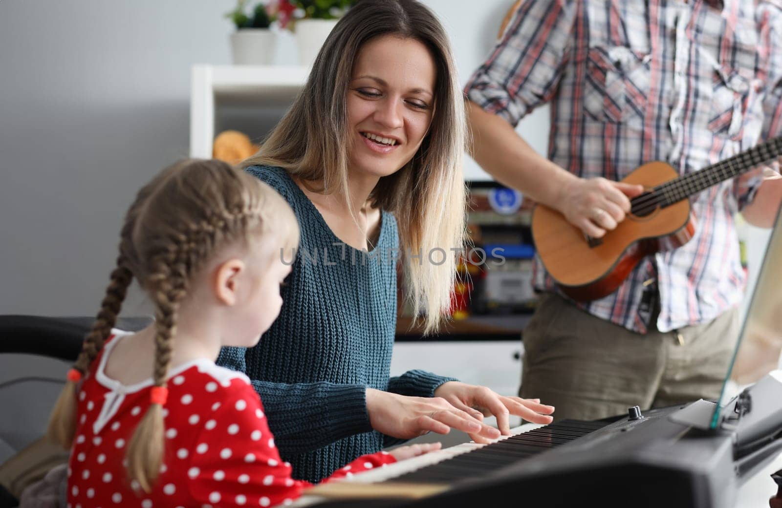 Woman and man teaching little girl to play musical instrument. Family fun concept