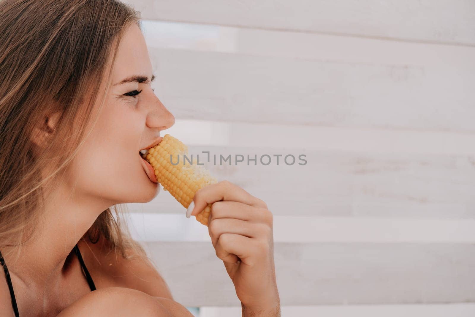 Woman eats corn on beach. Vegetarian hipster woman eat fresh organic grilled corn. Happy lady on sea beach sunset or ocean sunrise. Travel, explore, active yoga and meditation lifestyle concept. by panophotograph