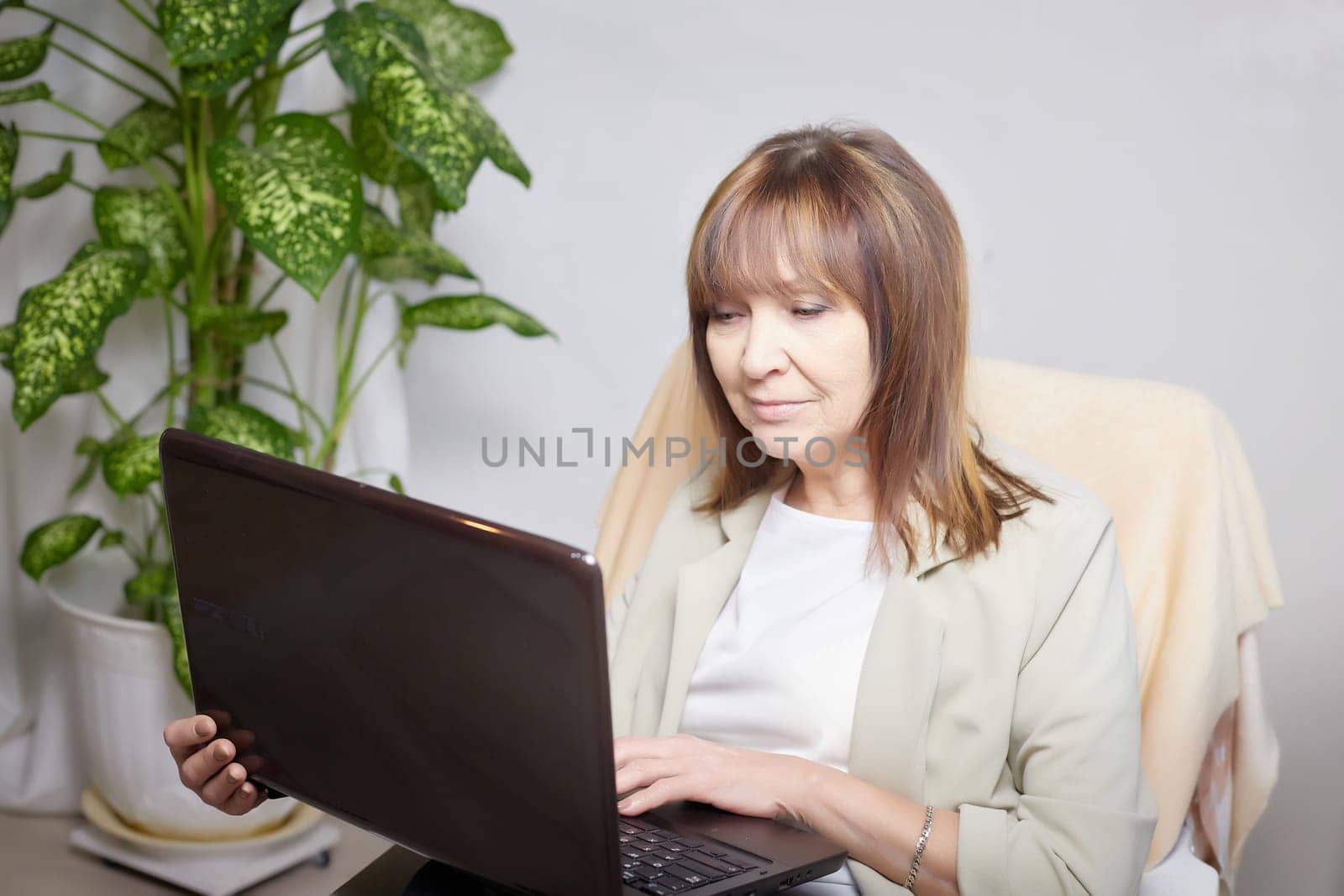 Elderly lady with a laptop in the room. A businesswoman is a leader, a manager is working. Grandma communicates with her grandchildren on the Internet