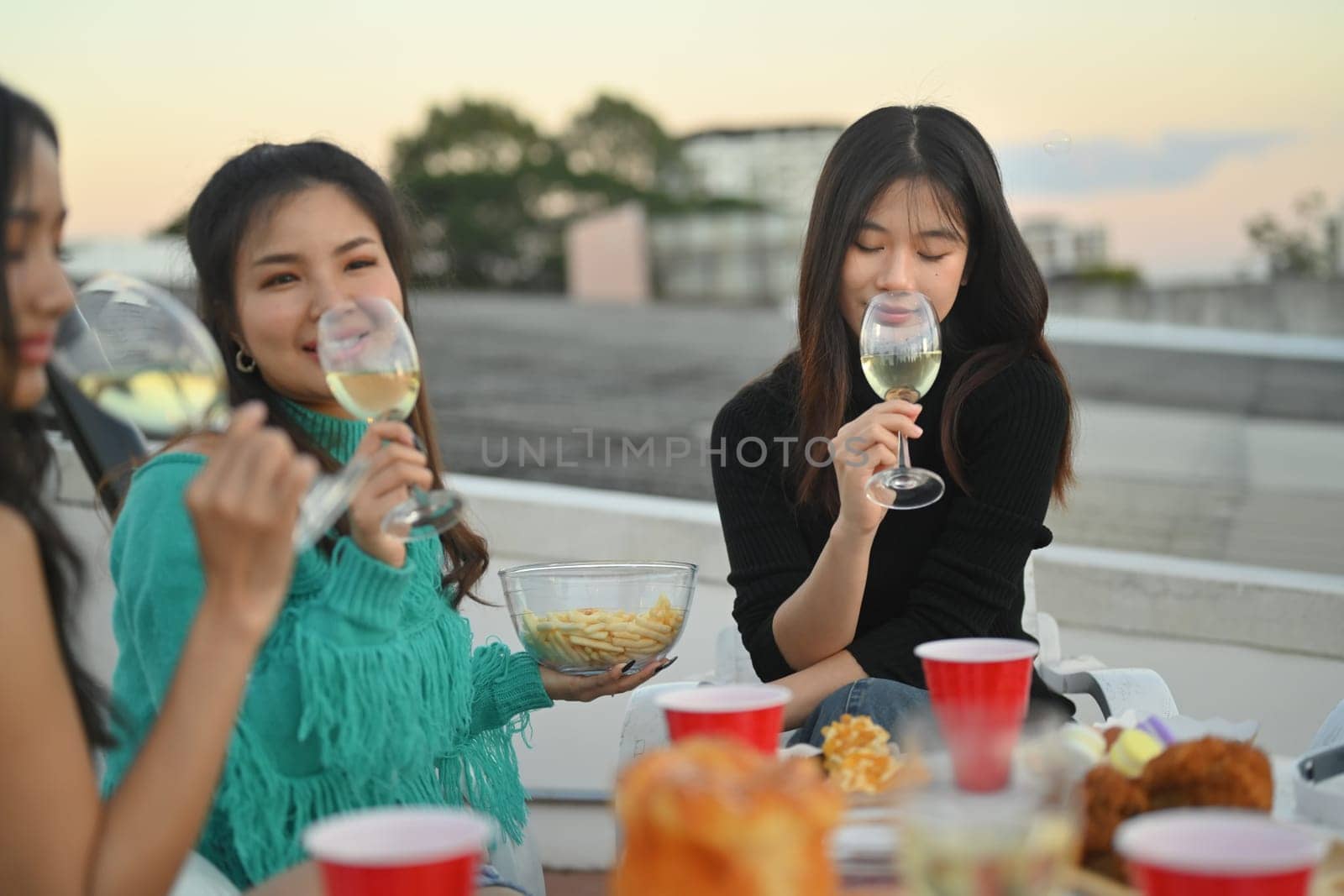 Young people hanging out on rooftop chatting and enjoying drinks. by prathanchorruangsak