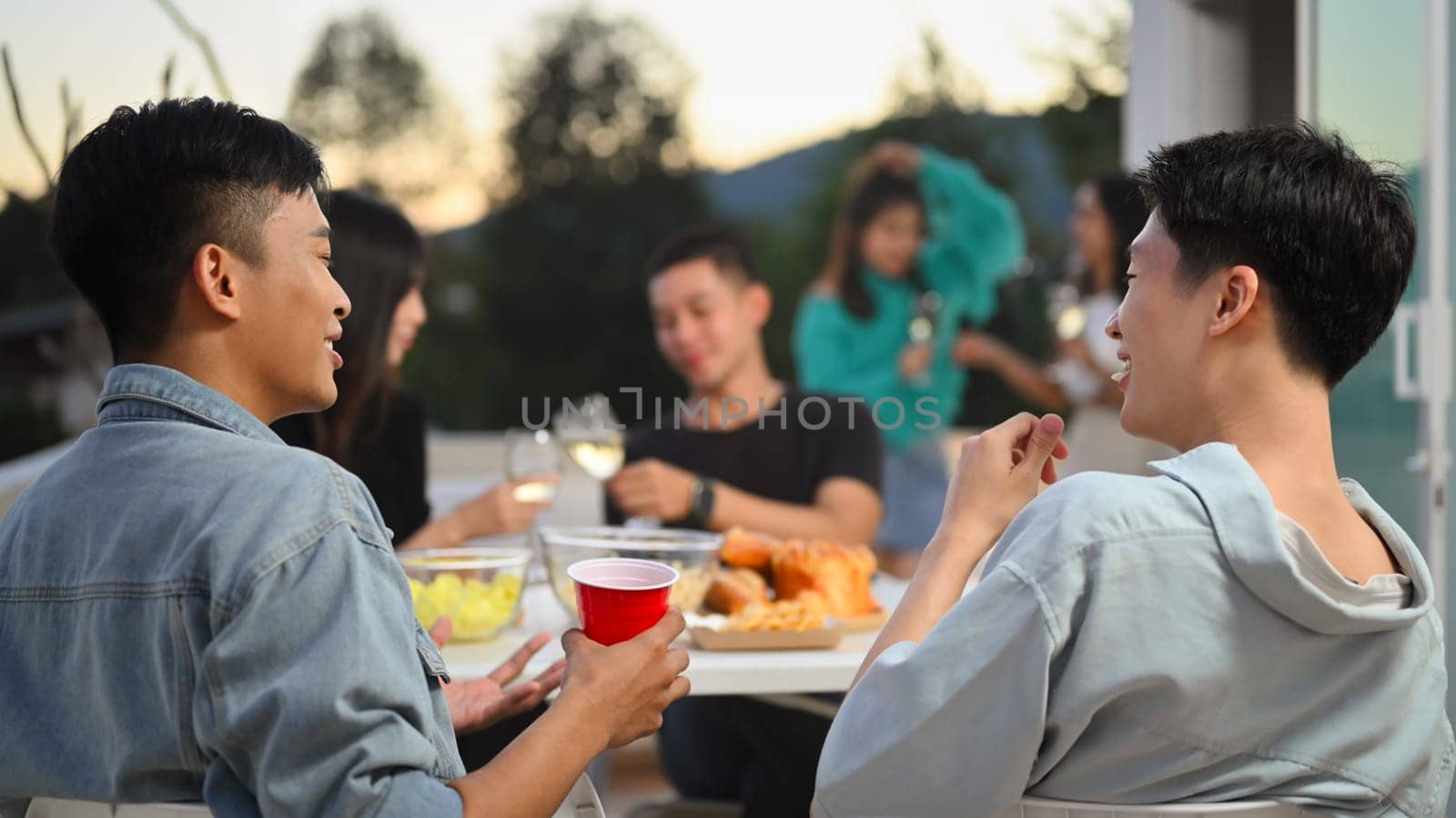 Happy friends having fun at outdoor rooftop party and chatting. Holiday celebration and friendship concept. by prathanchorruangsak