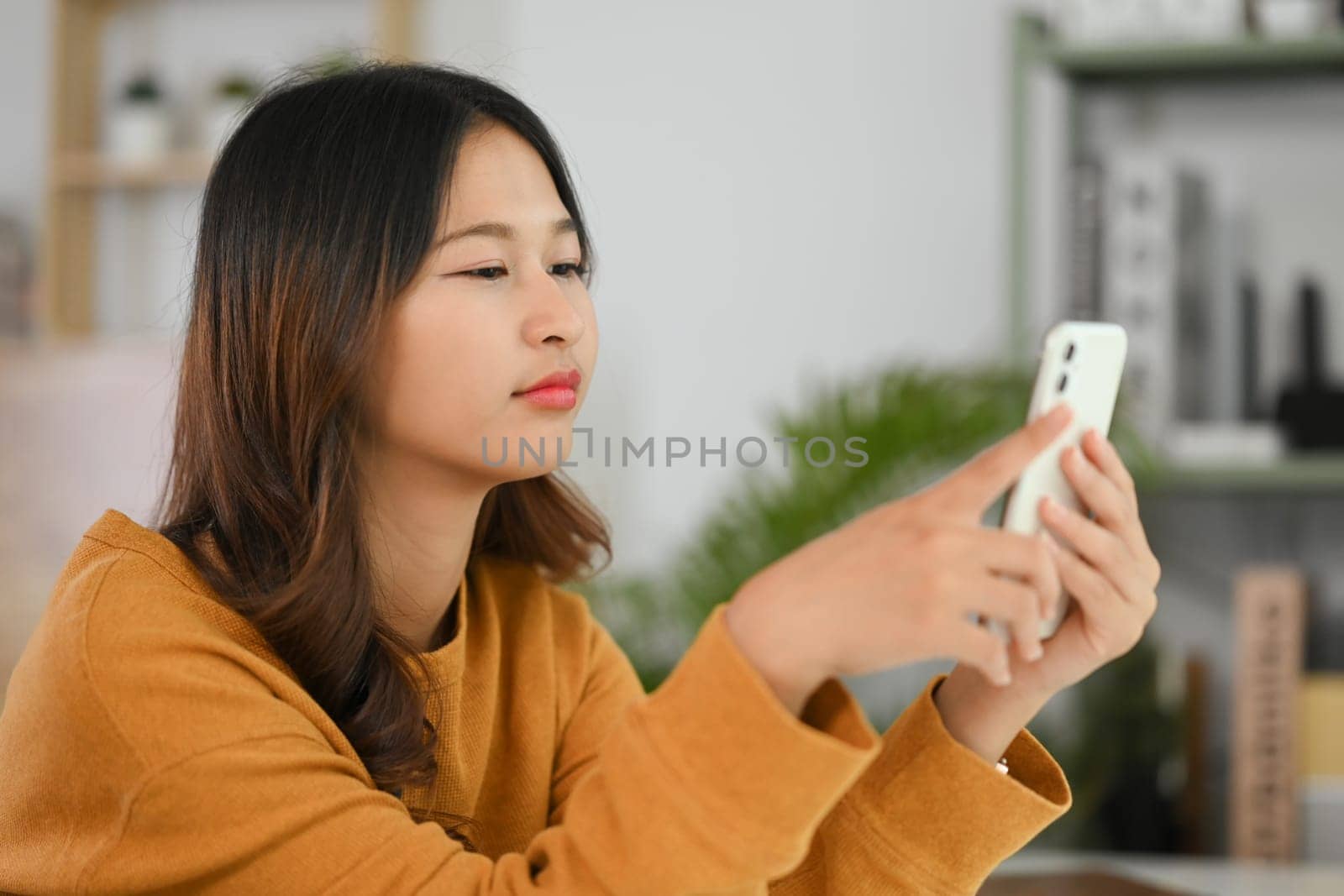 Pretty young Asian woman typing text message on mobile phone, chatting online